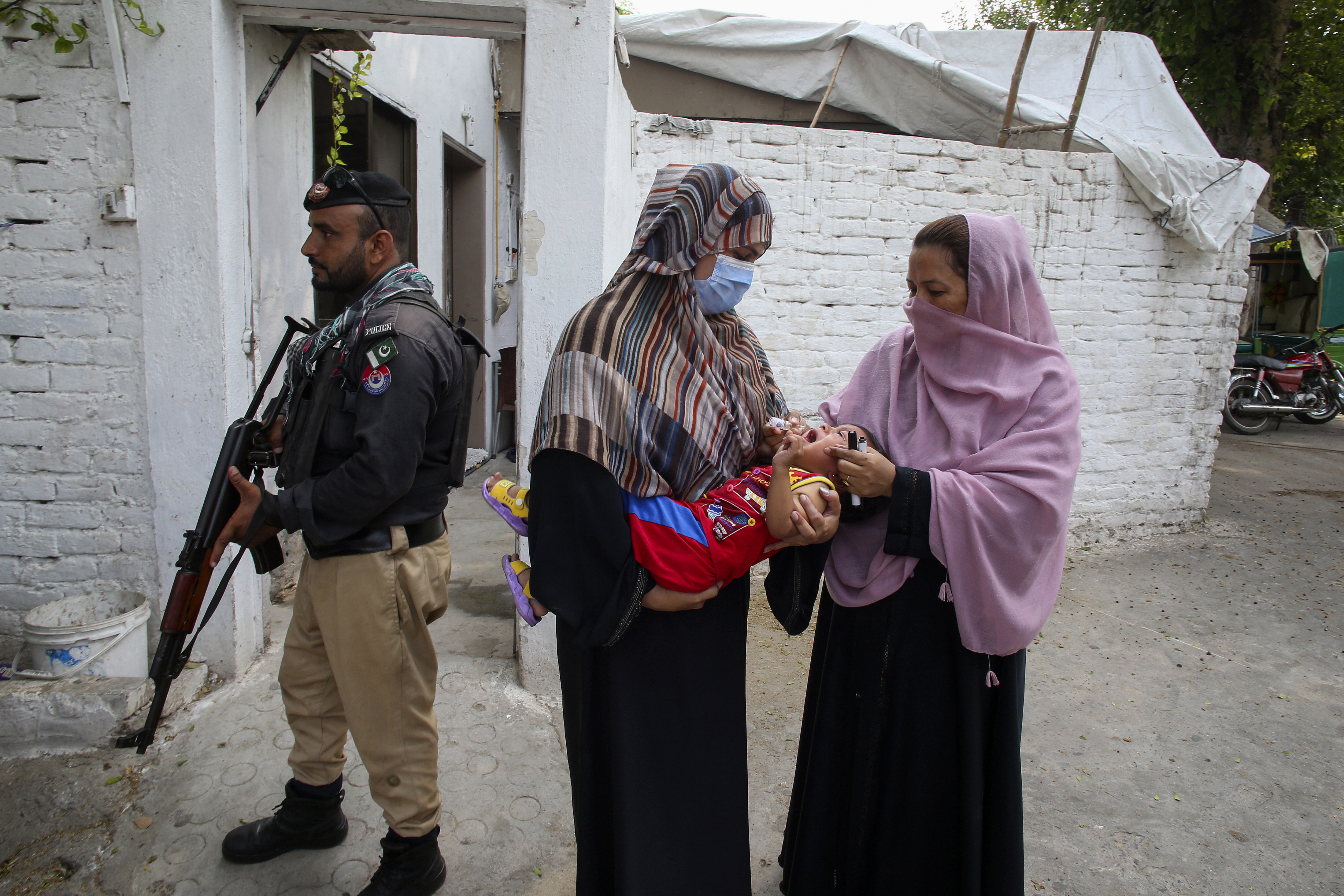 FILE -A police officer stands guard as a health worker, right, administers a polio vaccine to a child in a neighborhood of Peshawar, Pakistan, Sept. 9, 2024. (AP Photo/Muhammad Sajjad, File)