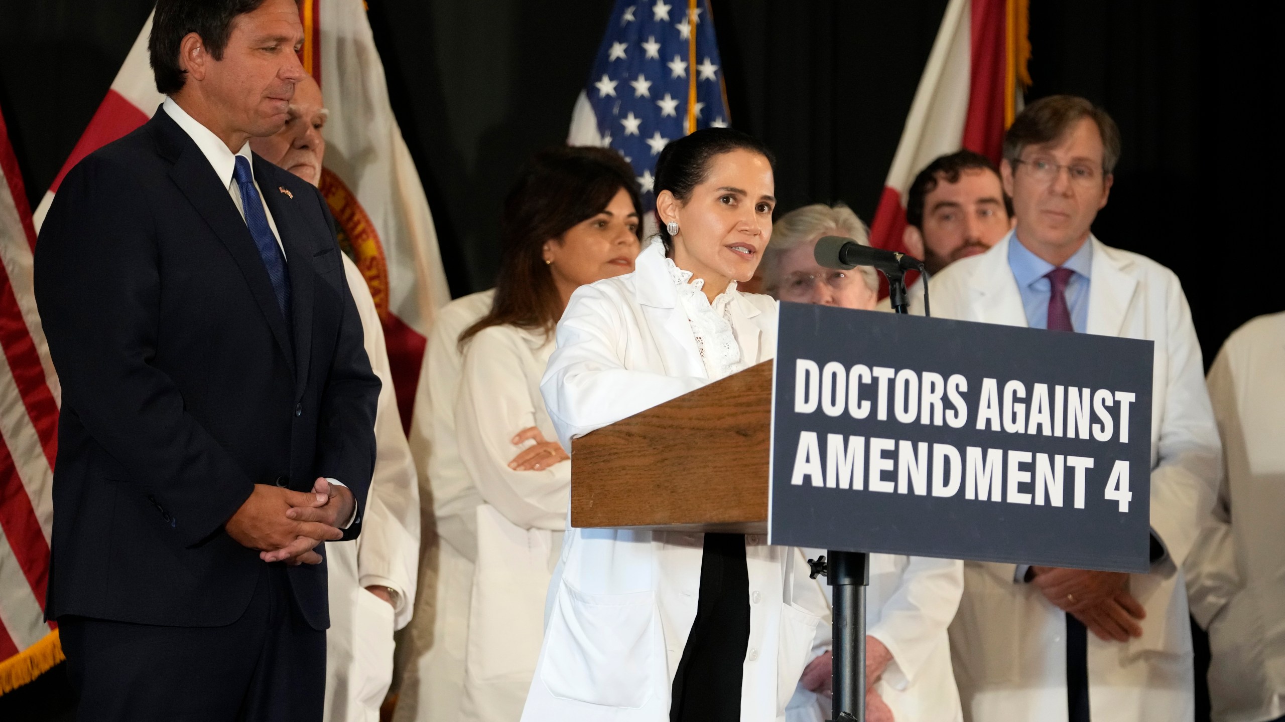 Dr. Christina Pena speaks during a news conference with Florida Physicians Against Amendment 4 as Florida Gov. Ron DeSantis, left, looks on Monday, Oct. 21, 2024, in Coral Gables, Fla. (AP Photo/Lynne Sladky)