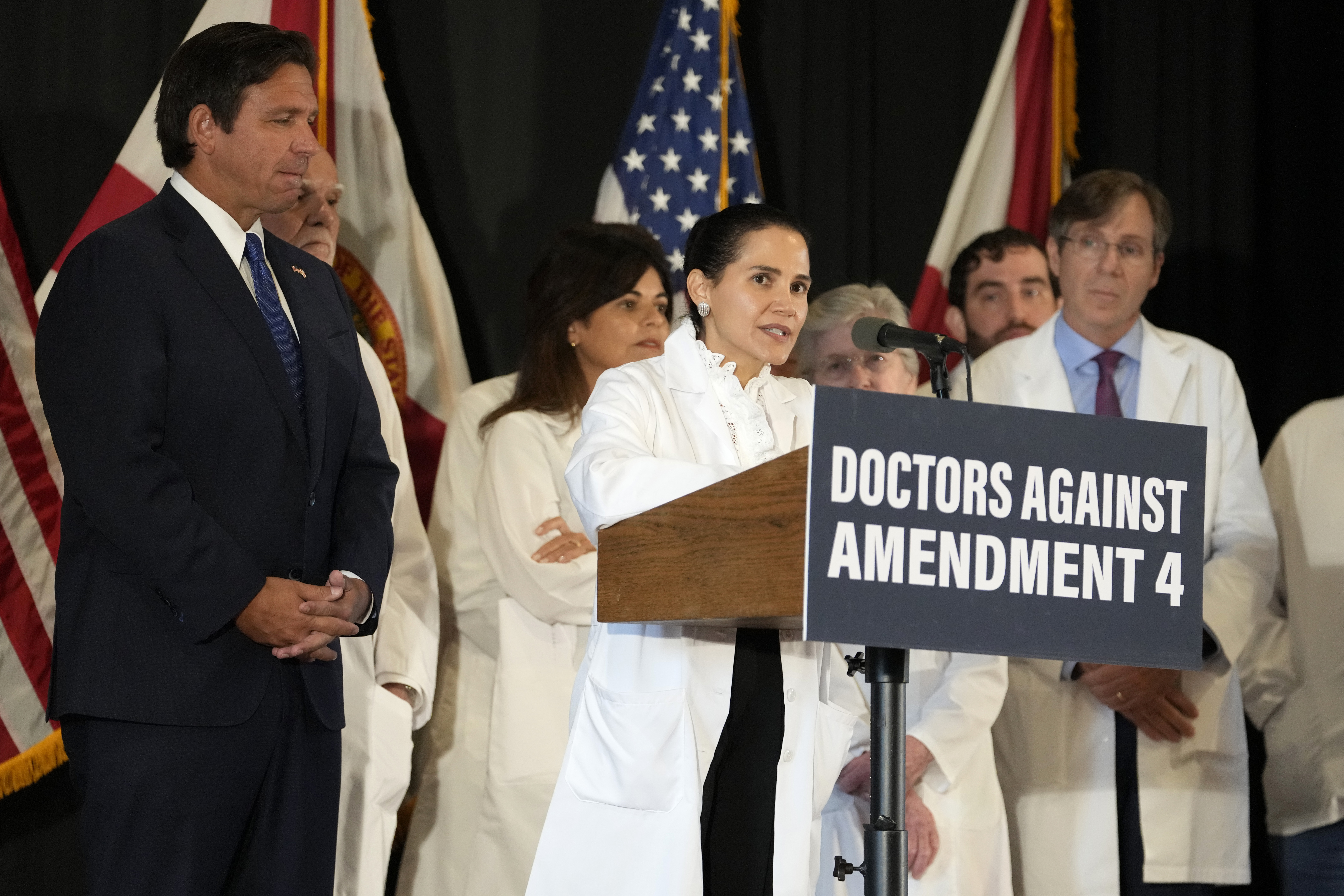 Dr. Christina Pena speaks during a news conference with Florida Physicians Against Amendment 4 as Florida Gov. Ron DeSantis, left, looks on Monday, Oct. 21, 2024, in Coral Gables, Fla. (AP Photo/Lynne Sladky)