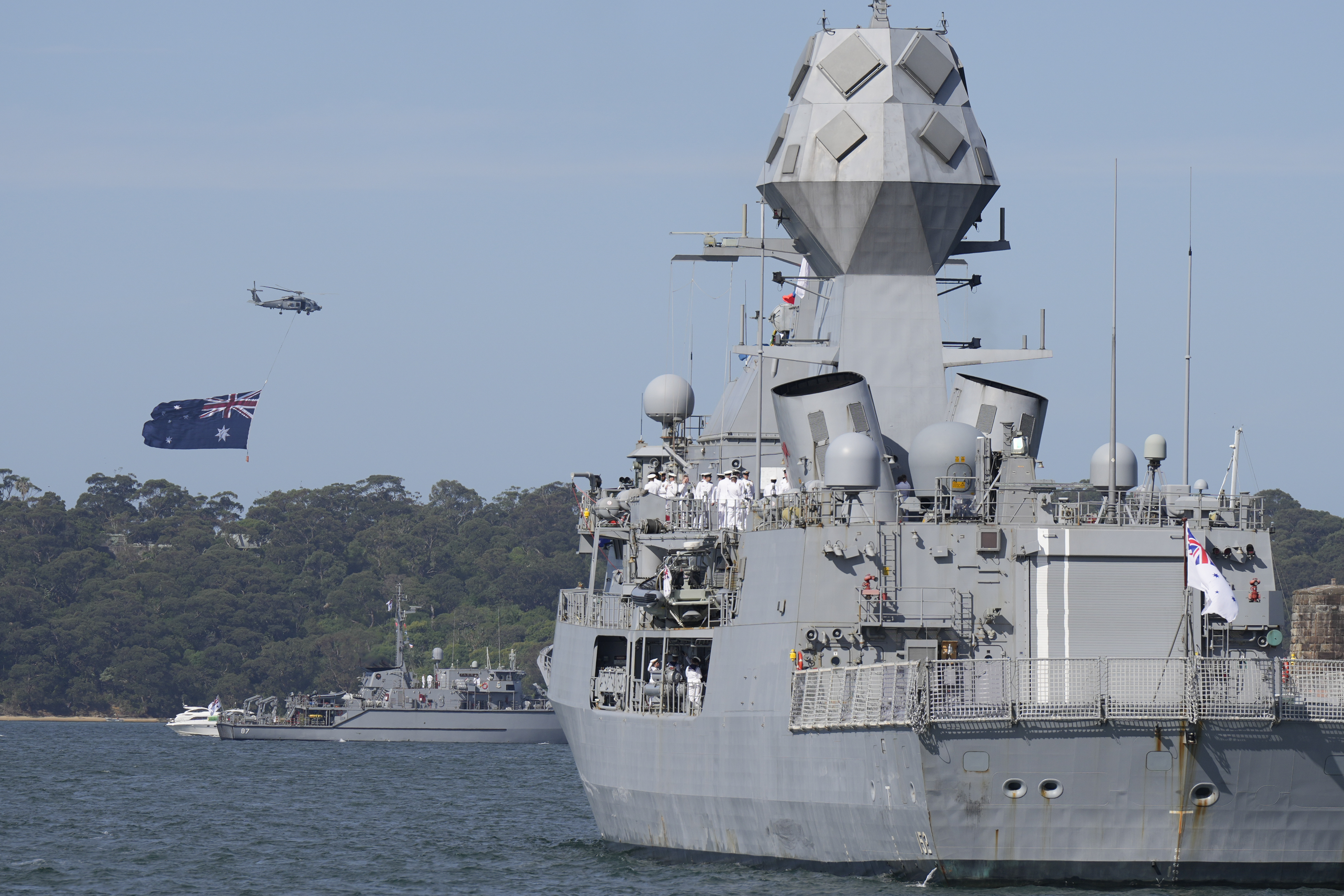 A helicopter flies with a giant Australian flag over the harbor ahead of Britain's King Charles III arrival at the Sydney Opera House in Sydney, Australia, Tuesday, Oct. 22, 2024. (AP Photo/Mark Baker, Pool)