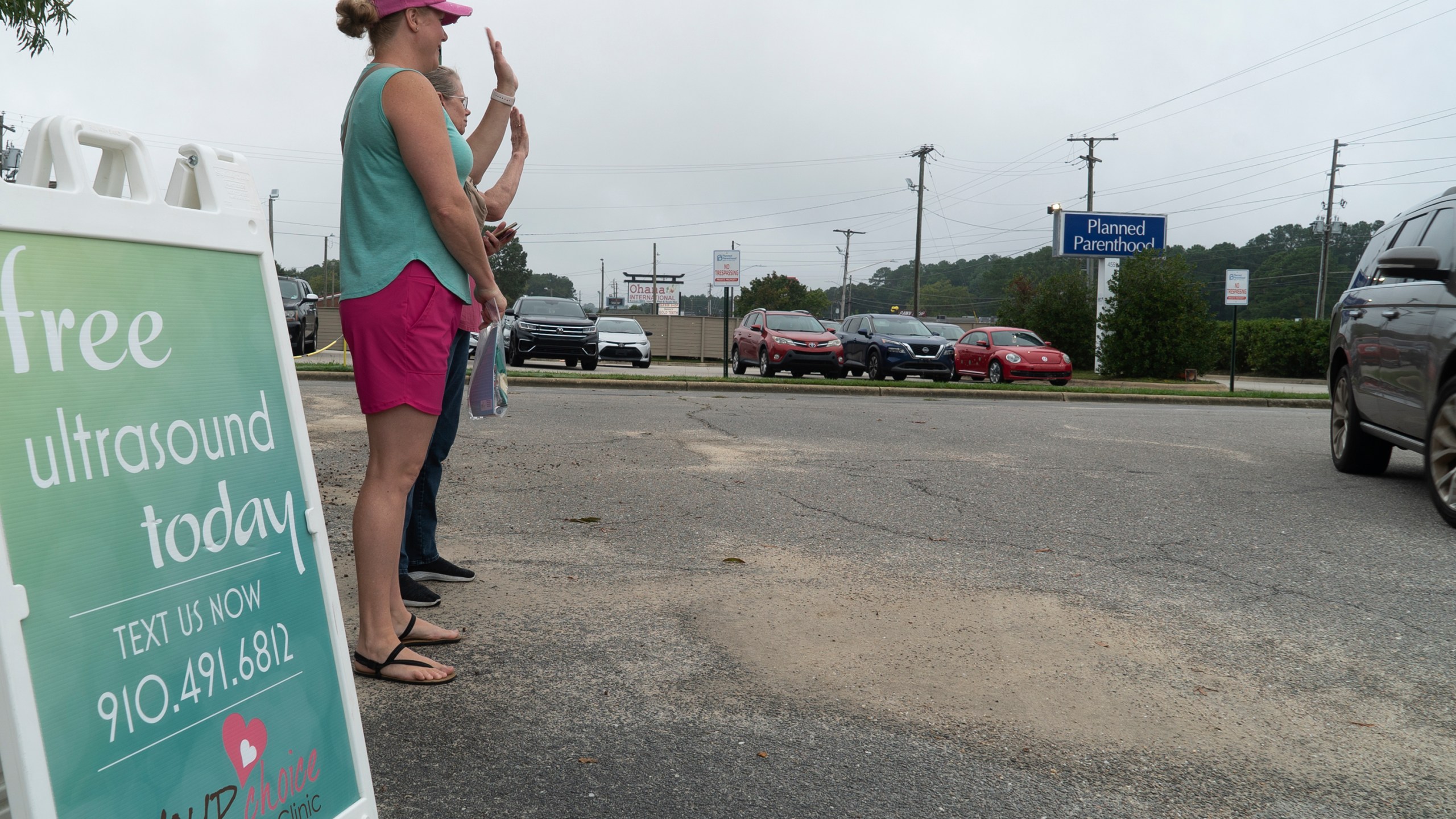 Air Force veteran and mother of two Laura Browne waves to a passing vehicle outside a Planned Parenthood clinic in Fayetteville, N.C., on Tuesday, Oct. 1, 2024. Browne does sidewalk ministry for a pregnancy center just up the road. (AP Photo/Allen G. Breed)