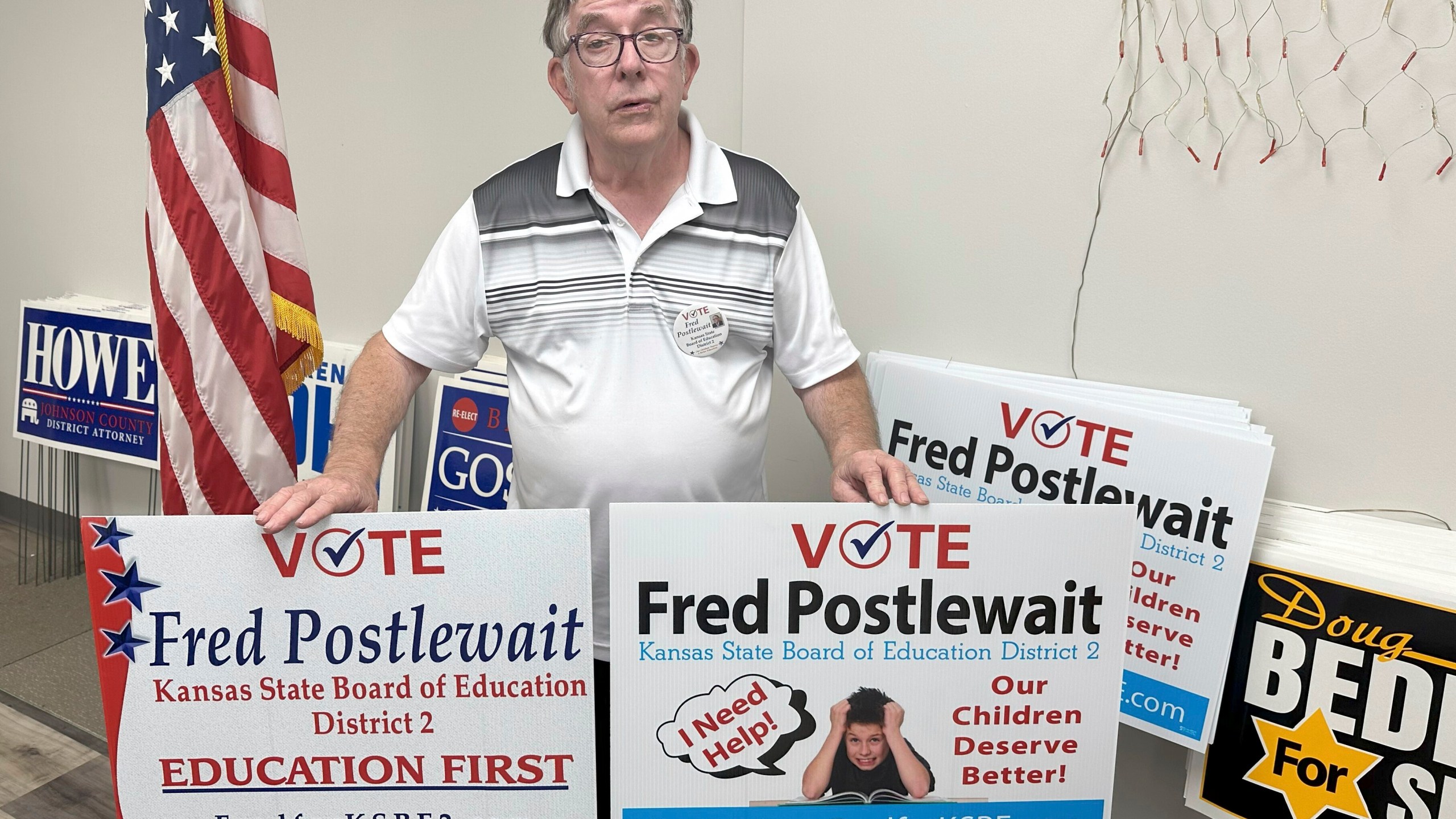 Fred Postlewait, a Republican candidate for the Kansas State Board of Education from Kansas City, Kan., shows off two of the yard signs available for supporters at the Republican Party's local headquarters in Johnson County, Tuesday, Oct. 1, 2024, in Overland Park, Kan. (AP Photo/John Hanna)