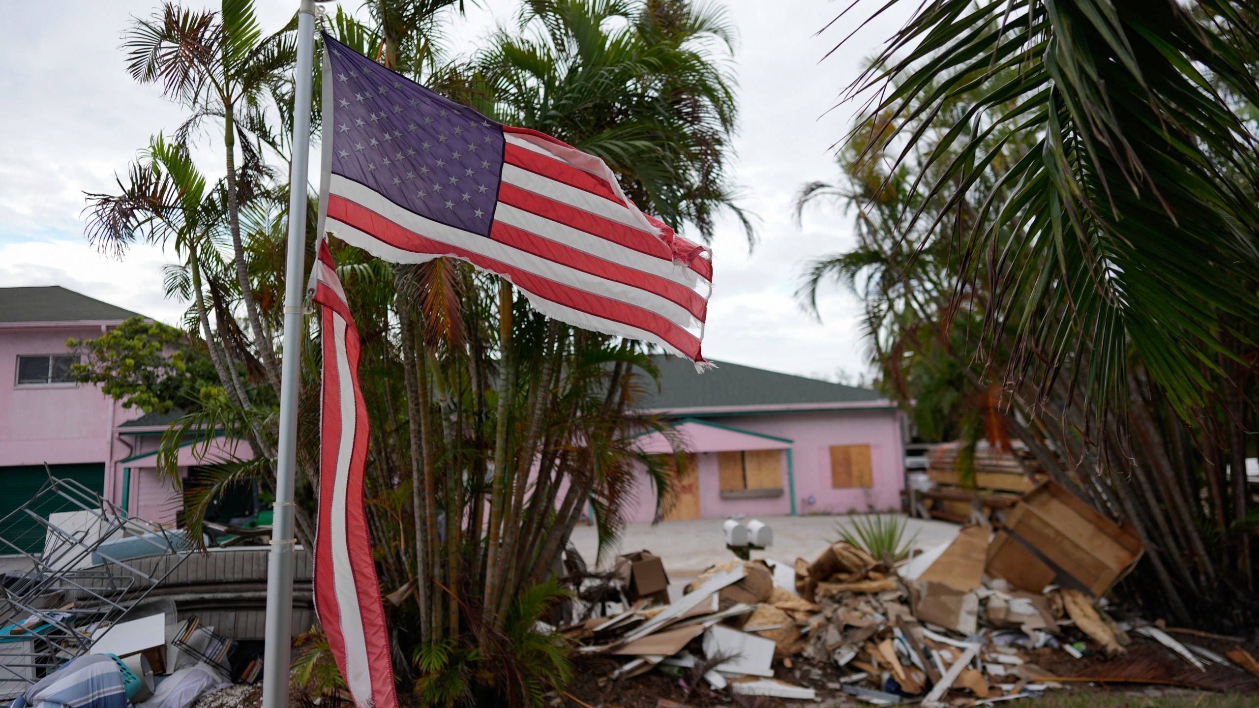 FILE - A tattered American flag flaps outside a home as furniture and household items damaged by Hurricane Helene flooding sit piled along the street awaiting pickup, ahead of the arrival of Hurricane Milton, in Holmes Beach on Anna Maria Island, Fla., Tuesday, Oct. 8, 2024. (AP Photo/Rebecca Blackwell, File)