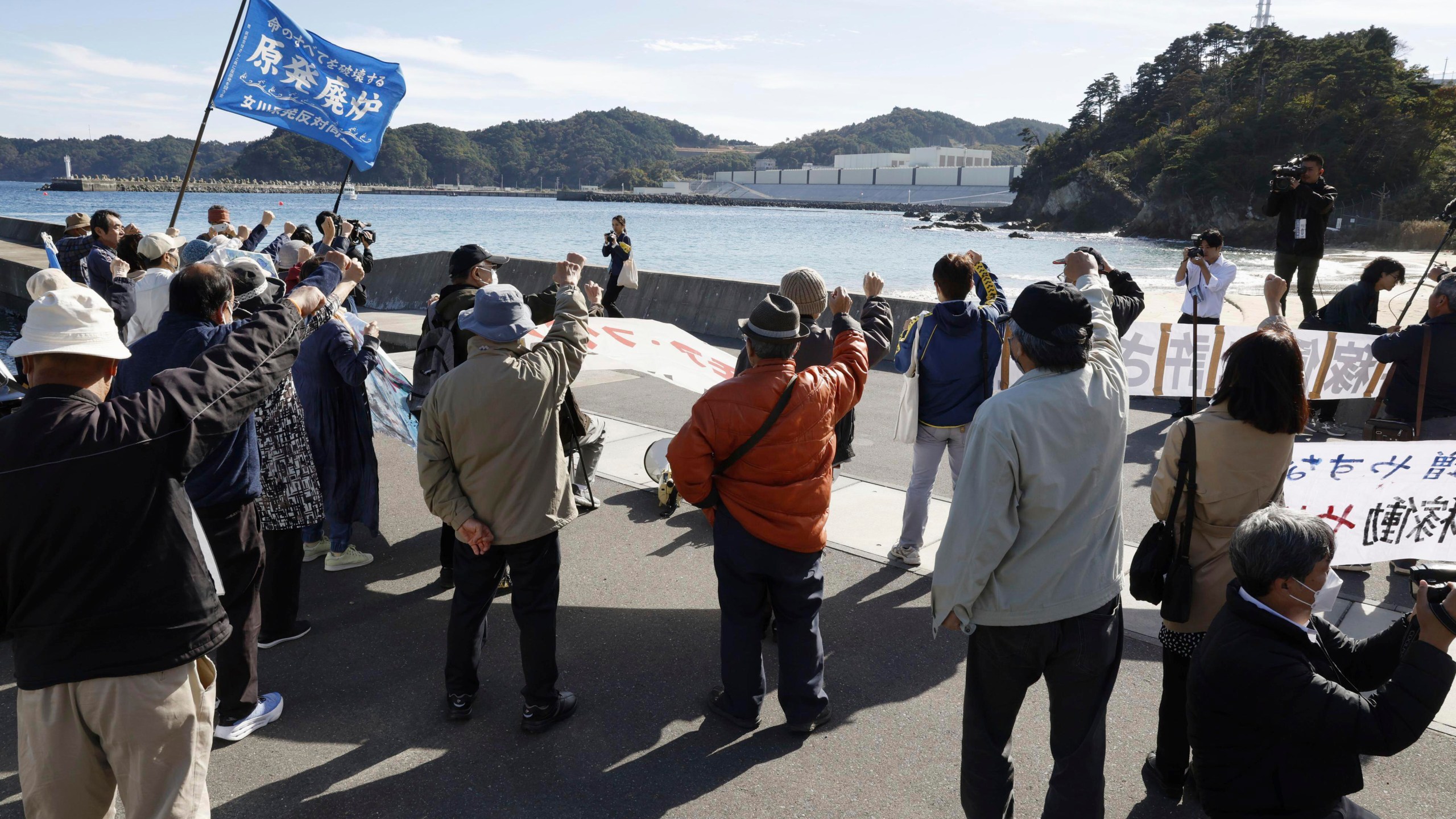 People protest against resuming operations of the Onagawa nuclear power plant, background, in Onagawa town, northeastern Japan, Tuesday, Oct. 29, 2024. (Miyuki Saito/Kyodo News via AP)