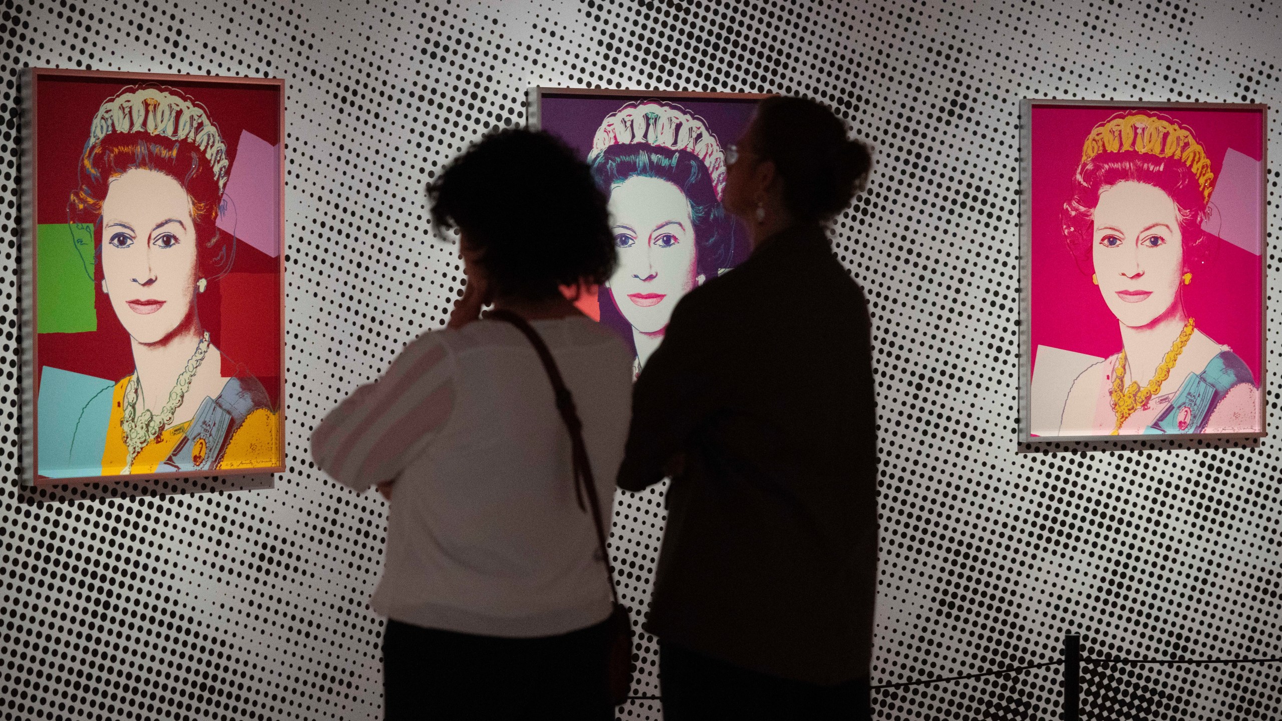 People look at screen print depicting Queen Elizabeth II, one in a series of sixteen prints of four queens titled Reigning Queens, 1985, by Andy Warhol at museum Paleis Het Loo in Apeldoorn, Netherlands, Wednesday, Oct. 9, 2024, similar to a Warhol work stolen from a gallery in Oisterwijk, Netherlands, early Friday, Nov. 1, 2024.(AP Photo/Peter Dejong)