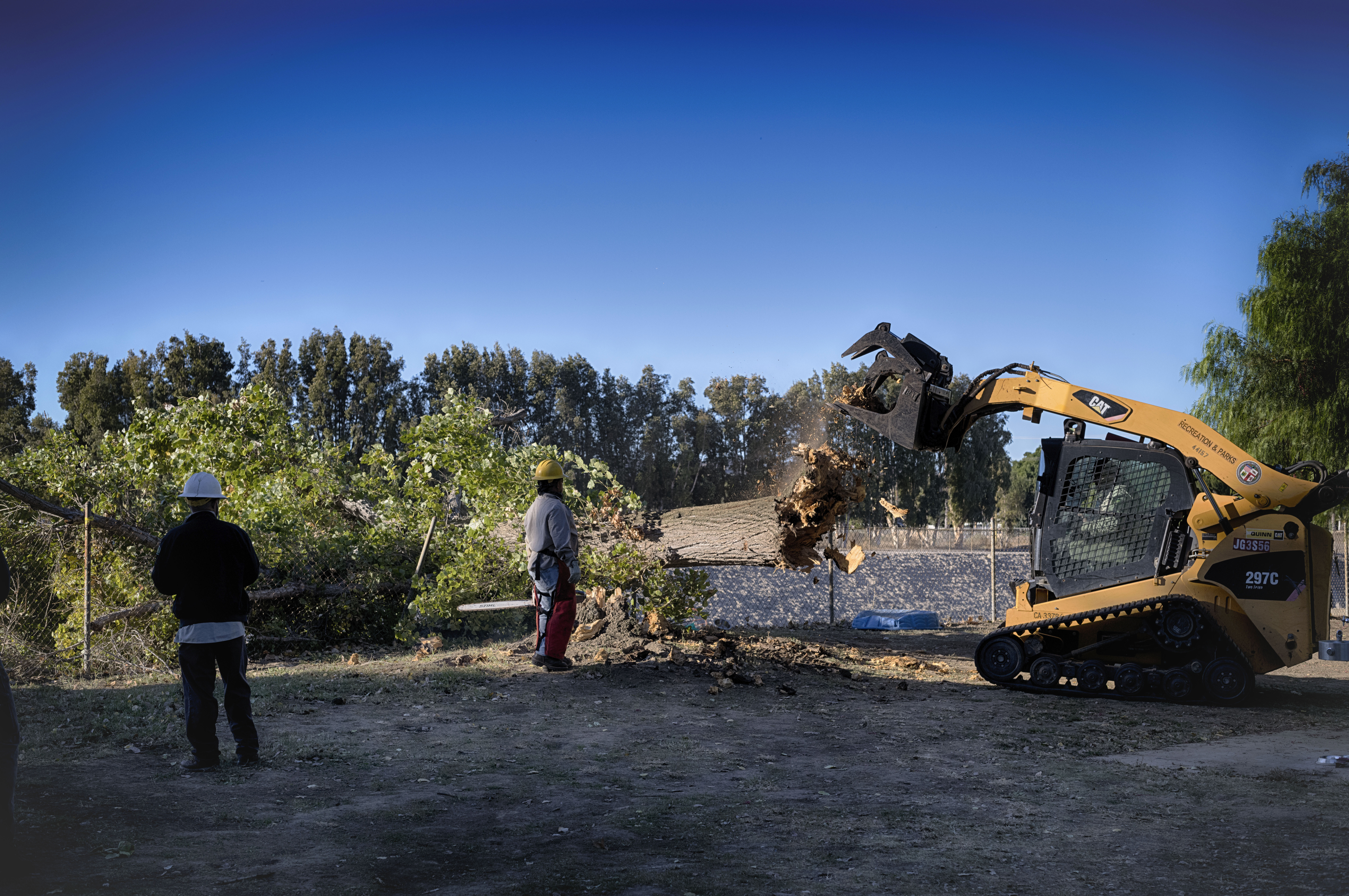 Los Angeles city workers remove the remains of a fallen tree blown over by intense winds that crushed a fence in a city park on Monday, Nov. 4, 2024. (AP Photo/Richard Vogel)