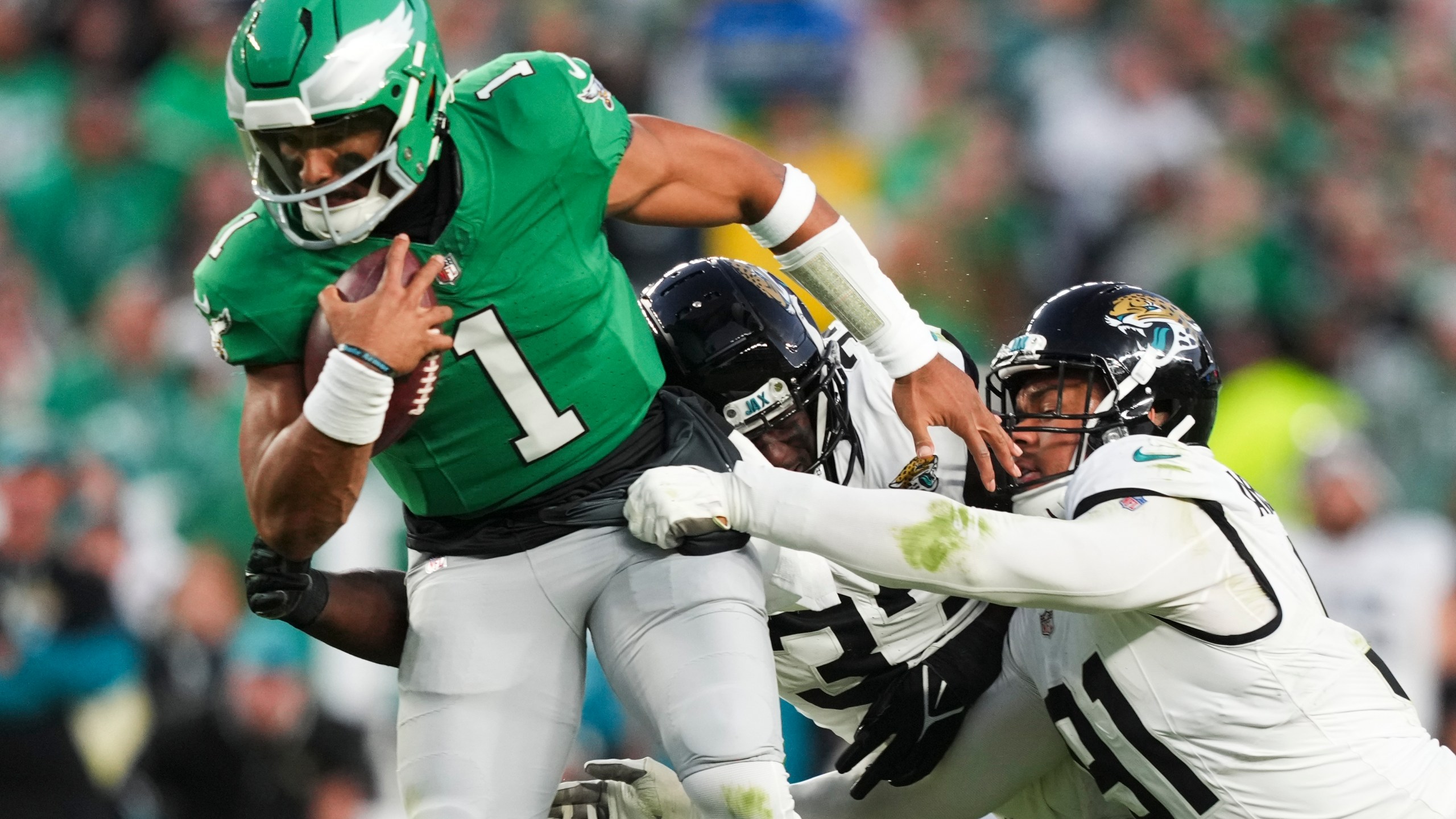 Philadelphia Eagles quarterback Jalen Hurts (1) scrambles under pressure from Jacksonville Jaguars linebacker Devin Lloyd, center, and Jaguars defensive end Arik Armstead during the first half of an NFL football game Sunday, Nov. 3, 2024, in Philadelphia. (AP Photo/Matt Slocum)