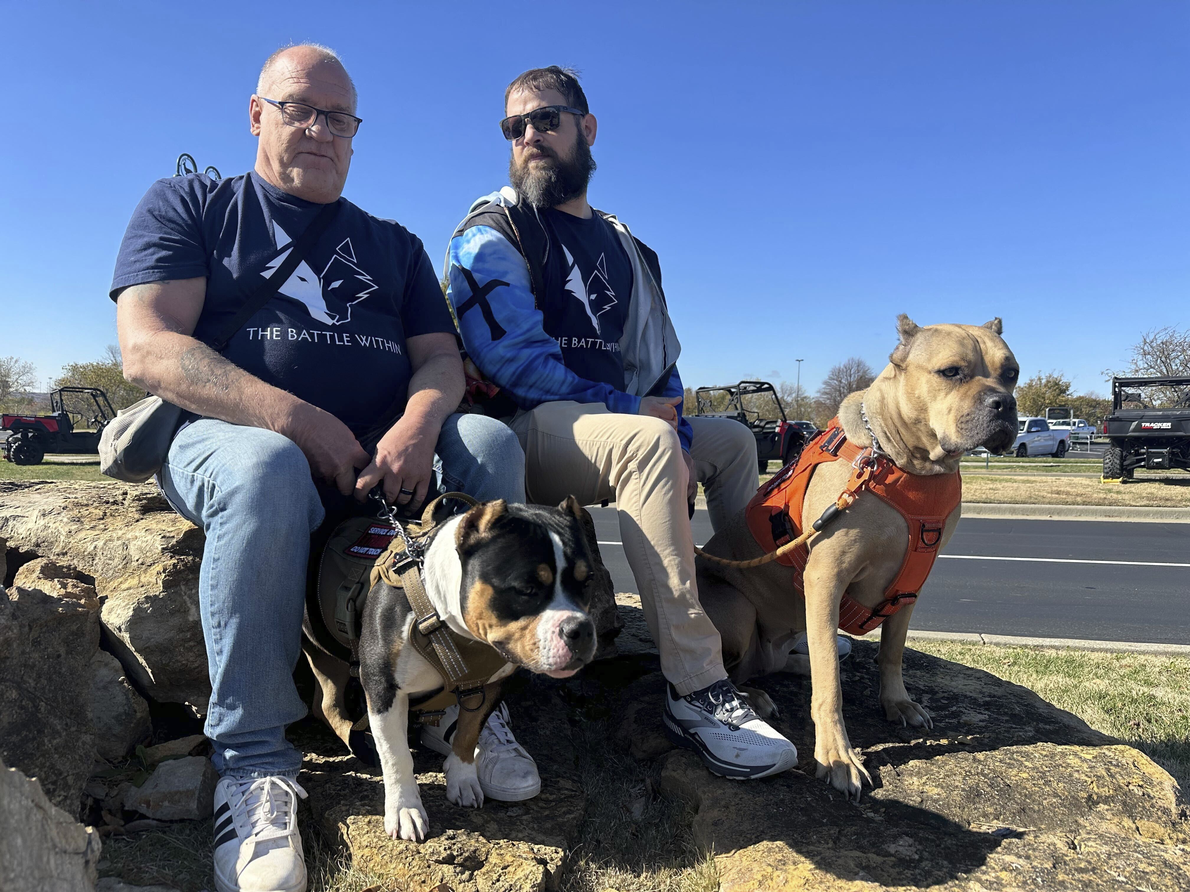 Retired Army First Sgt. Timothy Siebenmorgen, left, and retired Marine Corps Cpl. Mark Atkinson sit with their service dogs, Rosie and Lexi on Thursday, Nov. 7, 2024, in Kansas City, Kan., during a group training session. Both veterans are part of Dogs 4 Valor that helps retired veterans and first responders in the Kansas City area work with their service dogs to help manage depression, anxiety and other challenges. (AP Photo/Nick Ingram)