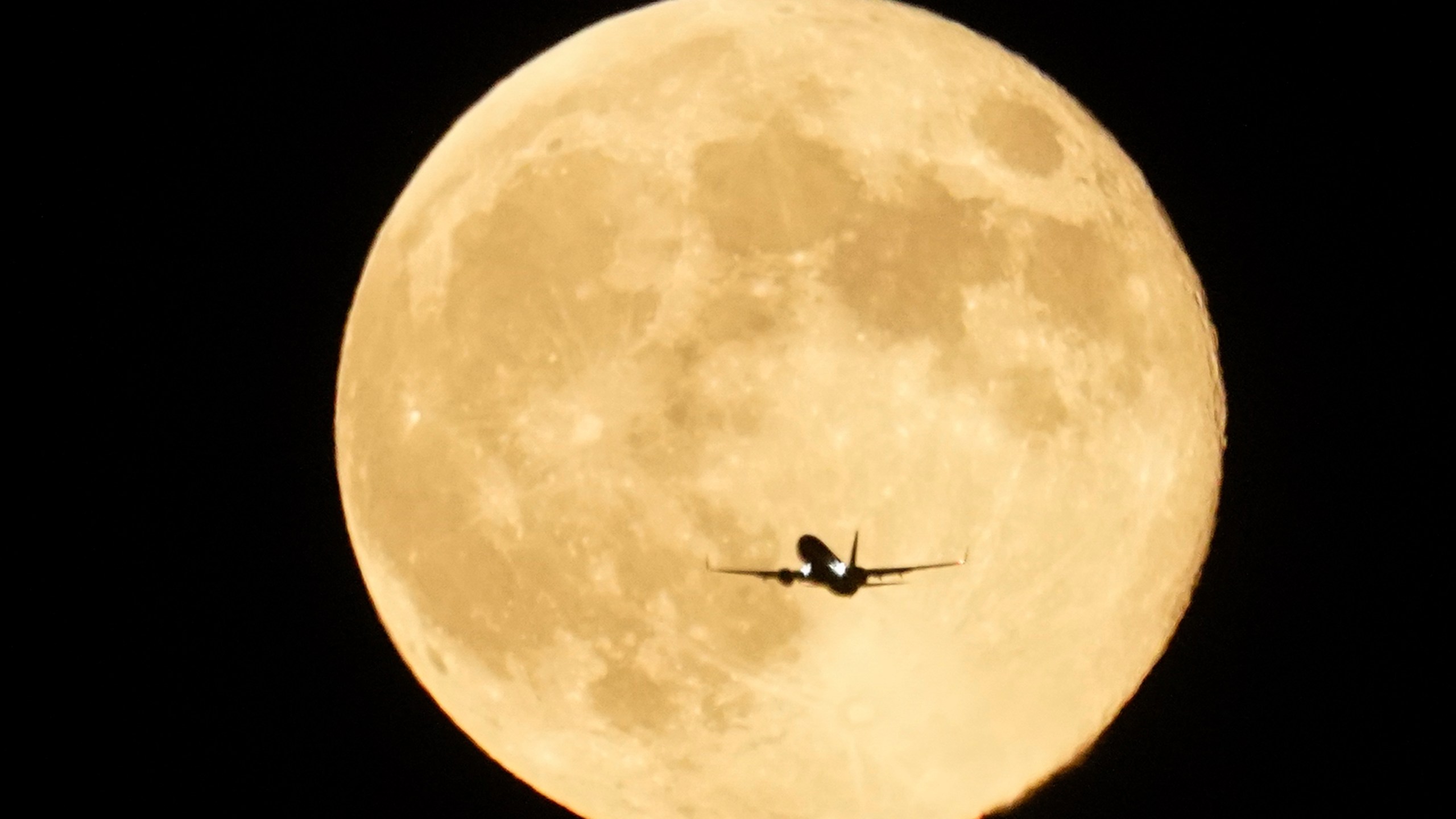 An airplane flies past the moon as it rises over Lake Michigan, Thursday, Oct. 17, 2024, in Chicago. (AP Photo/Kiichiro Sato)