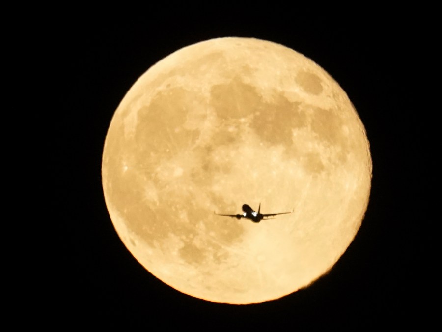 An airplane flies past the moon as it rises over Lake Michigan, Thursday, Oct. 17, 2024, in Chicago. (AP Photo/Kiichiro Sato)