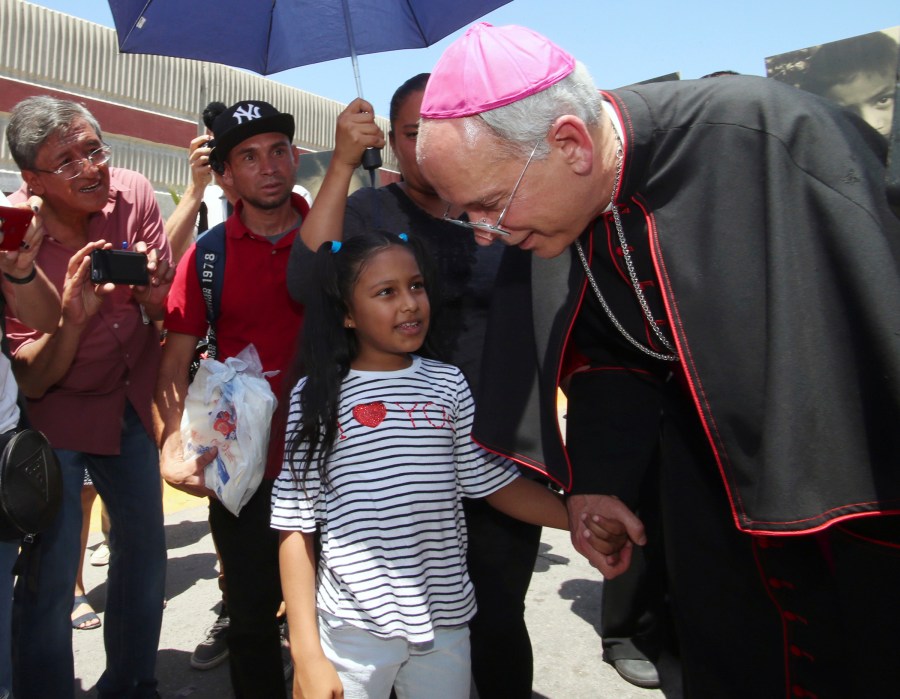 FILE - El Paso Catholic Bishop Mark Seitz talks with Celsia Palma, 9, of Honduras, as they walk to the Paso Del Norte International Port of Entry, Thursday, June, 27, 2019, in Juarez, Mexico. (AP Photo/Rudy Gutierrez, File)