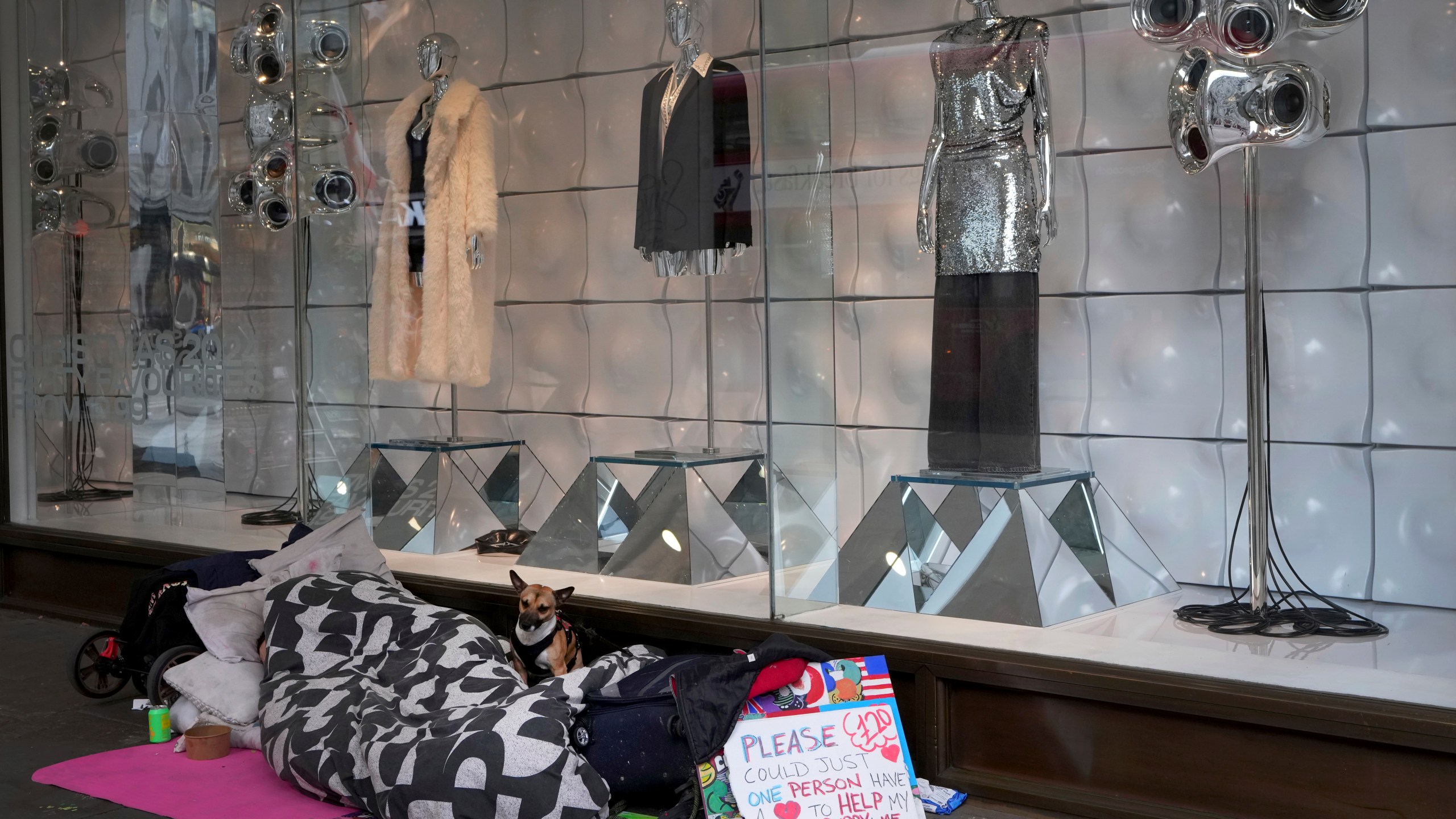 A man sleeps alongside his dog outside a festive shop window in Oxford Street in London, Friday, Nov. 15, 2024. (AP Photo/Kirsty Wigglesworth)