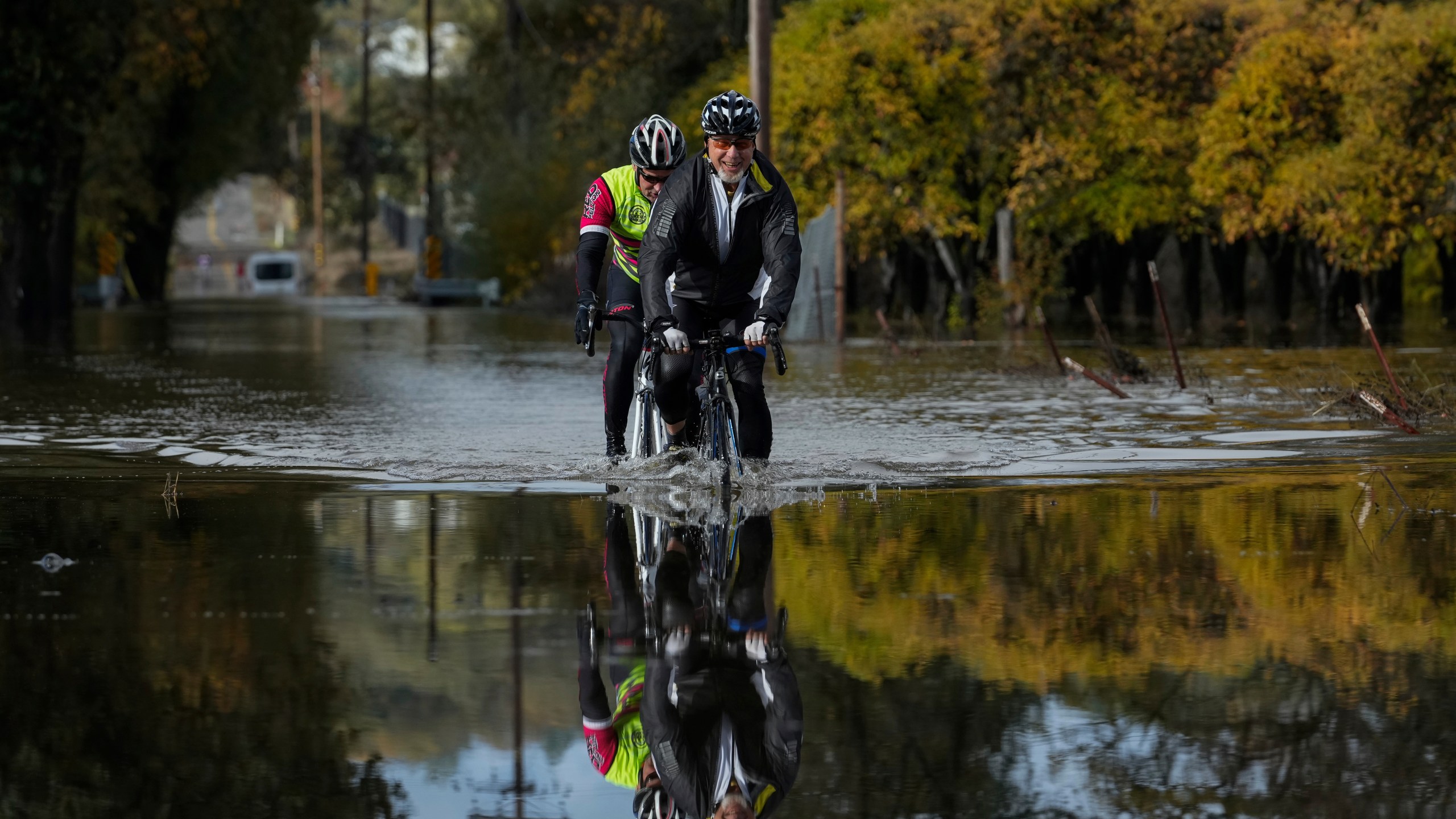 Dave Edmonds, right, and Mike Raasch ride their bicycles on a flooded road Saturday, Nov. 23, 2024, in Windsor, Calif. (AP Photo/Godofredo A. Vásquez)