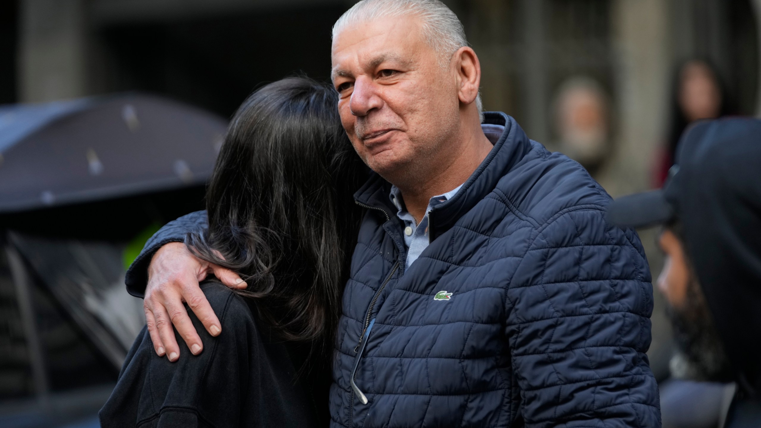 A man comforts her daughter as they look at their destroyed building where they were living, which was hit Sunday night in an Israeli airstrike in Dahiyeh, in the southern suburb of Beirut, Lebanon, Monday, Nov. 25, 2024. (AP Photo/Hussein Malla)