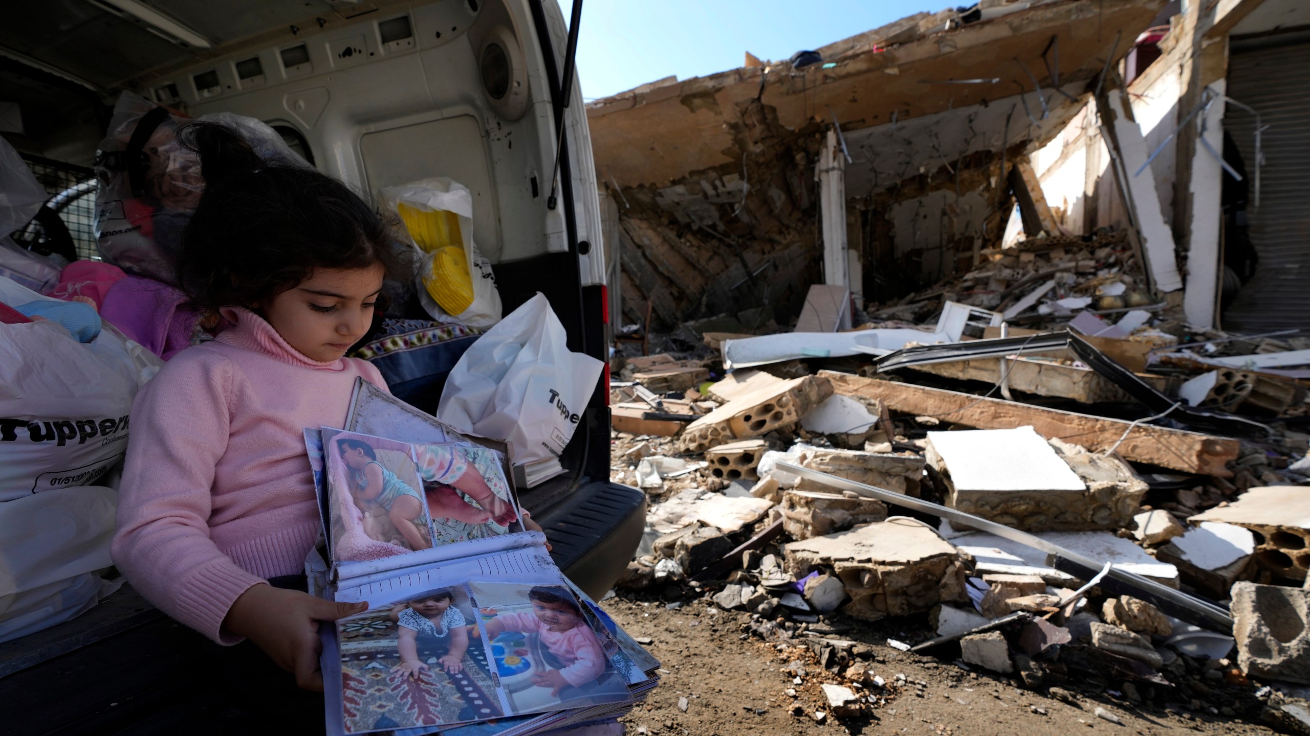 Yara Srour, 4, holds her photo album, as she sits in front of her grandparents destroyed house after she returned with her family to Hanouiyeh village, southern Lebanon, Thursday, Nov. 28, 2024 following a ceasefire between Israel and Hezbollah that went into effect on Wednesday.(AP Photo/Hussein Malla)