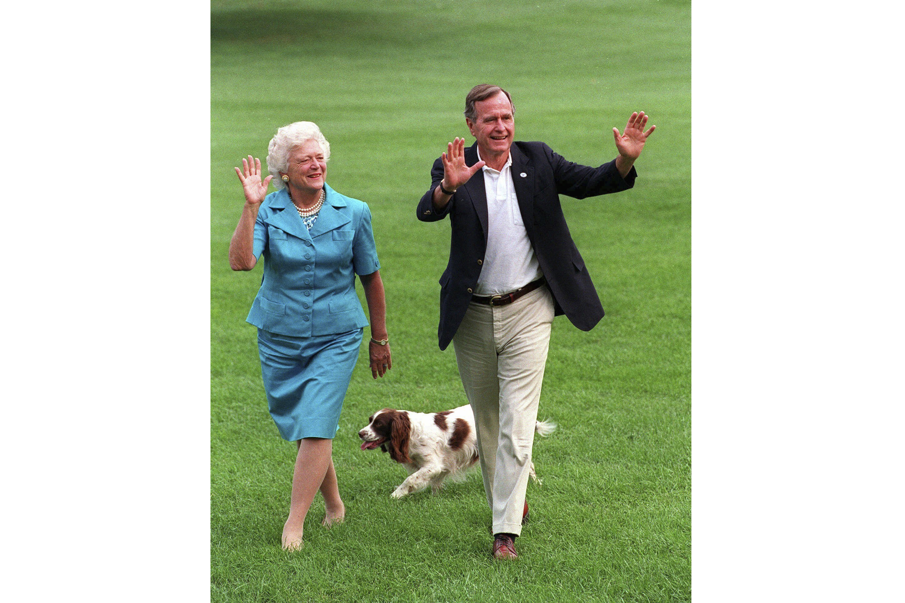 FILE- President Bush, right, and first lady Barbara Bush walking with their dog Millie across the South Lawn as they return to the White House, Aug. 24, 1992. (AP Photo/Scott Applewhite, File)