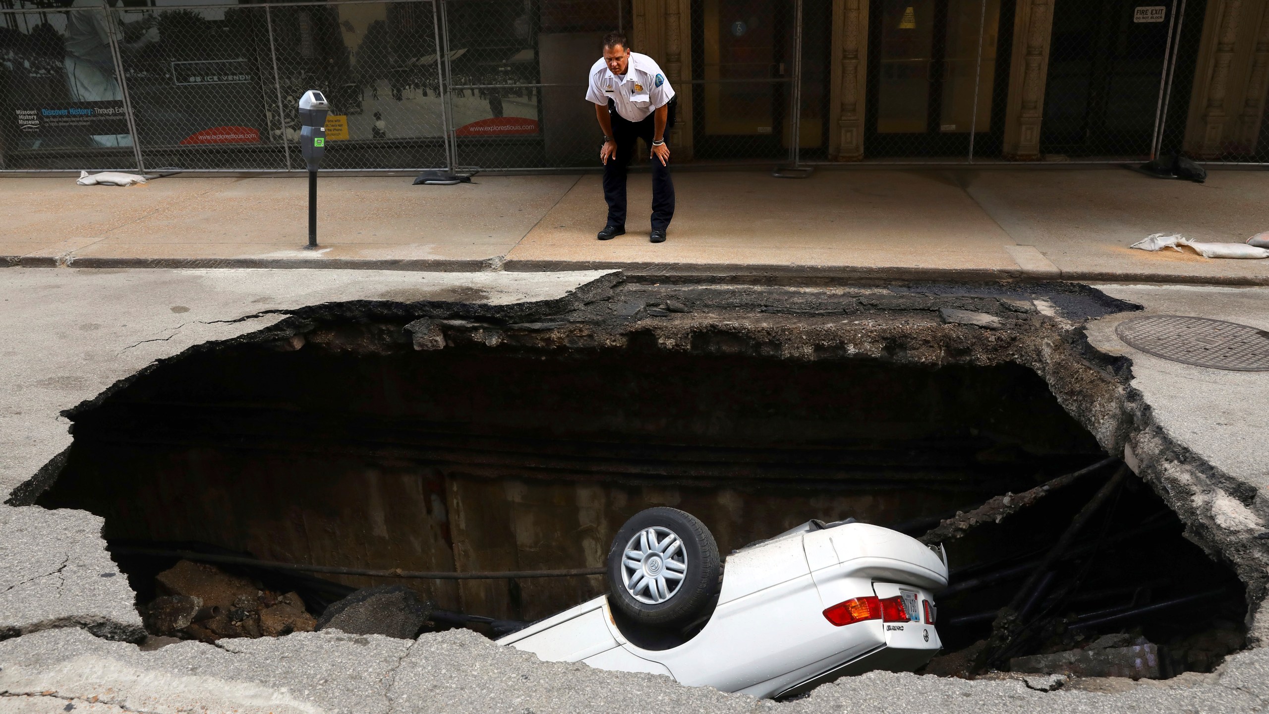 FILE - A St. Louis police officer looks over a large hole in 6th Street, Thursday, June 29, 2017, in St. Louis, that swallowed a Toyota Camry between Olive and Locust Streets. (Christian Gooden/St. Louis Post-Dispatch via AP, File)