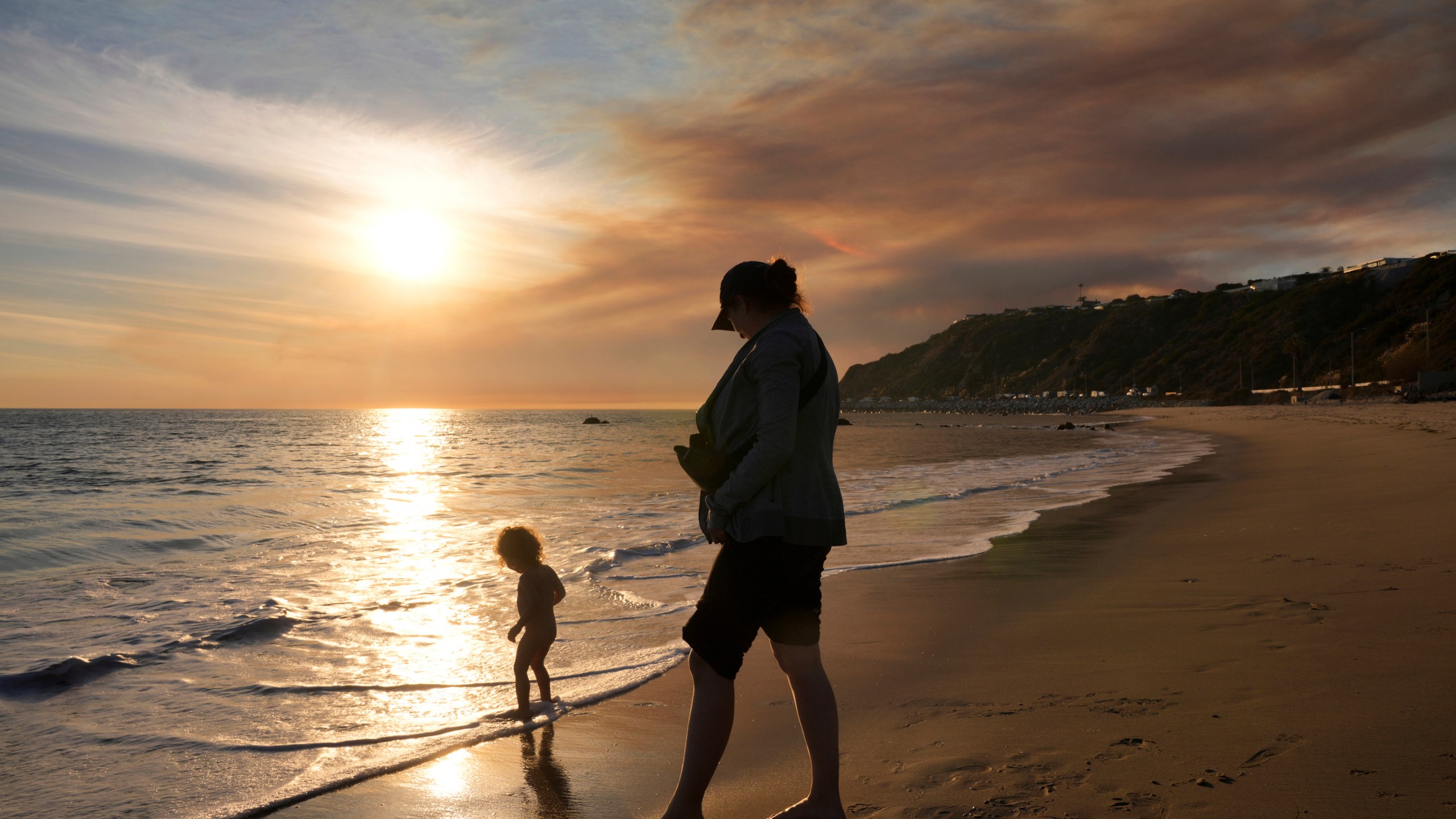 Malibu residents Florence Johnson and her son Brian enjoy the beach before sunset as a plume of smoke from the Franklin Fire rises over the ocean Tuesday, Dec. 10, 2024, in Malibu, Calif. (AP Photo/Damian Dovarganes)