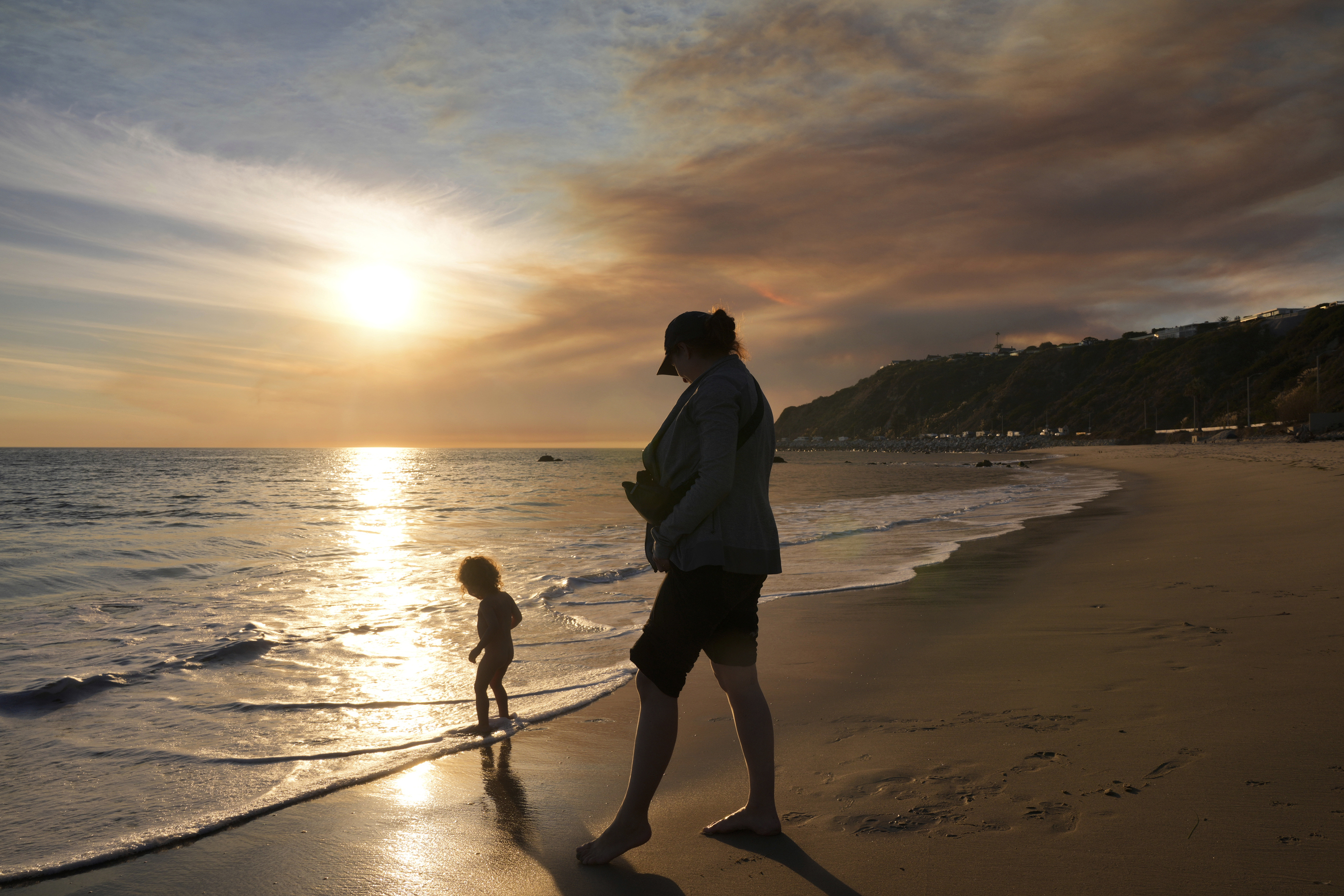 Malibu residents Florence Johnson and her son Brian enjoy the beach before sunset as a plume of smoke from the Franklin Fire rises over the ocean Tuesday, Dec. 10, 2024, in Malibu, Calif. (AP Photo/Damian Dovarganes)