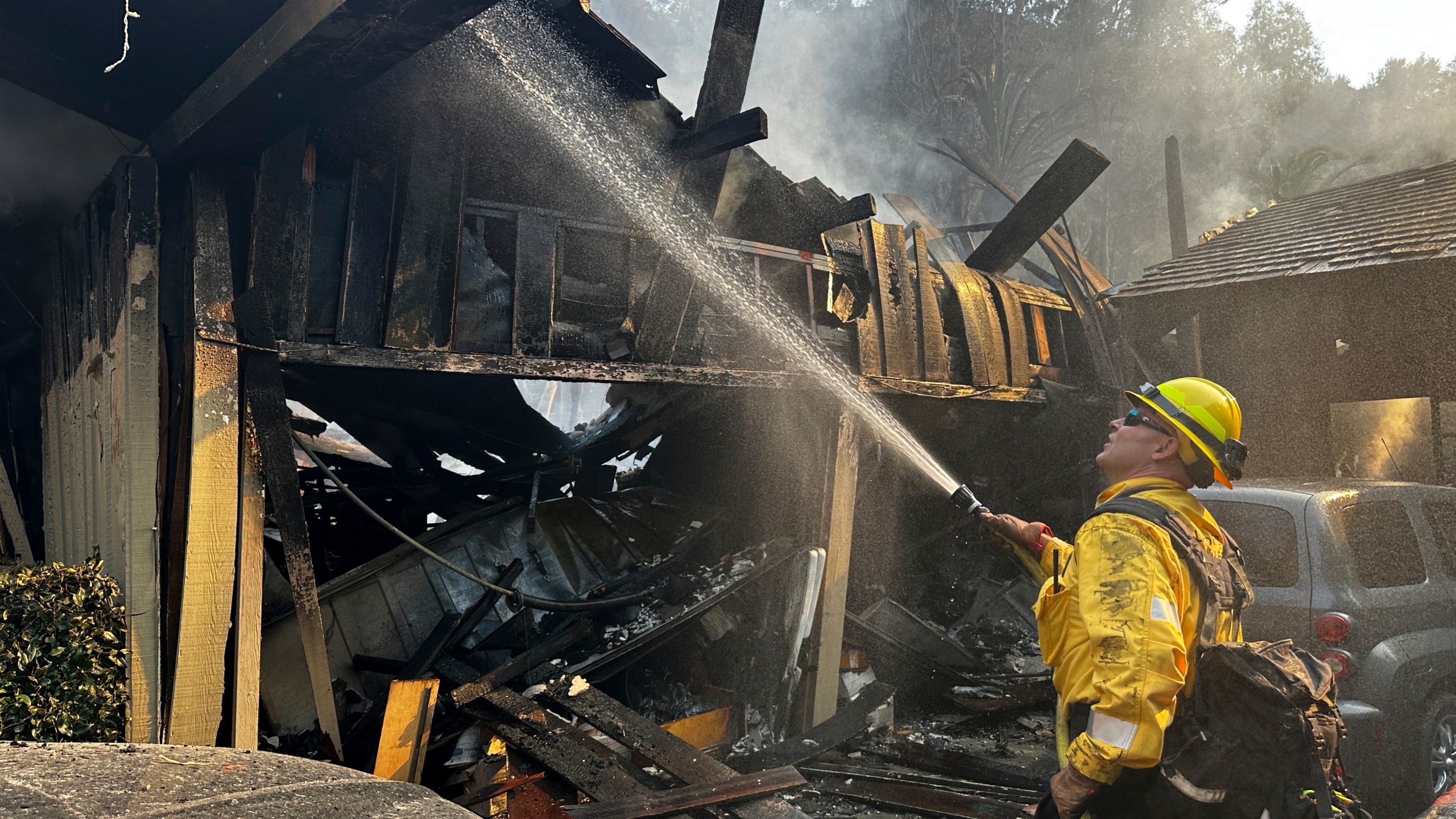 A firefighter hoses down hot spots around a fire-ravaged property after the Franklin Fire swept through Tuesday, Dec. 10, 2024, in Malibu, Calif. (AP Photo/Eugene Garcia)