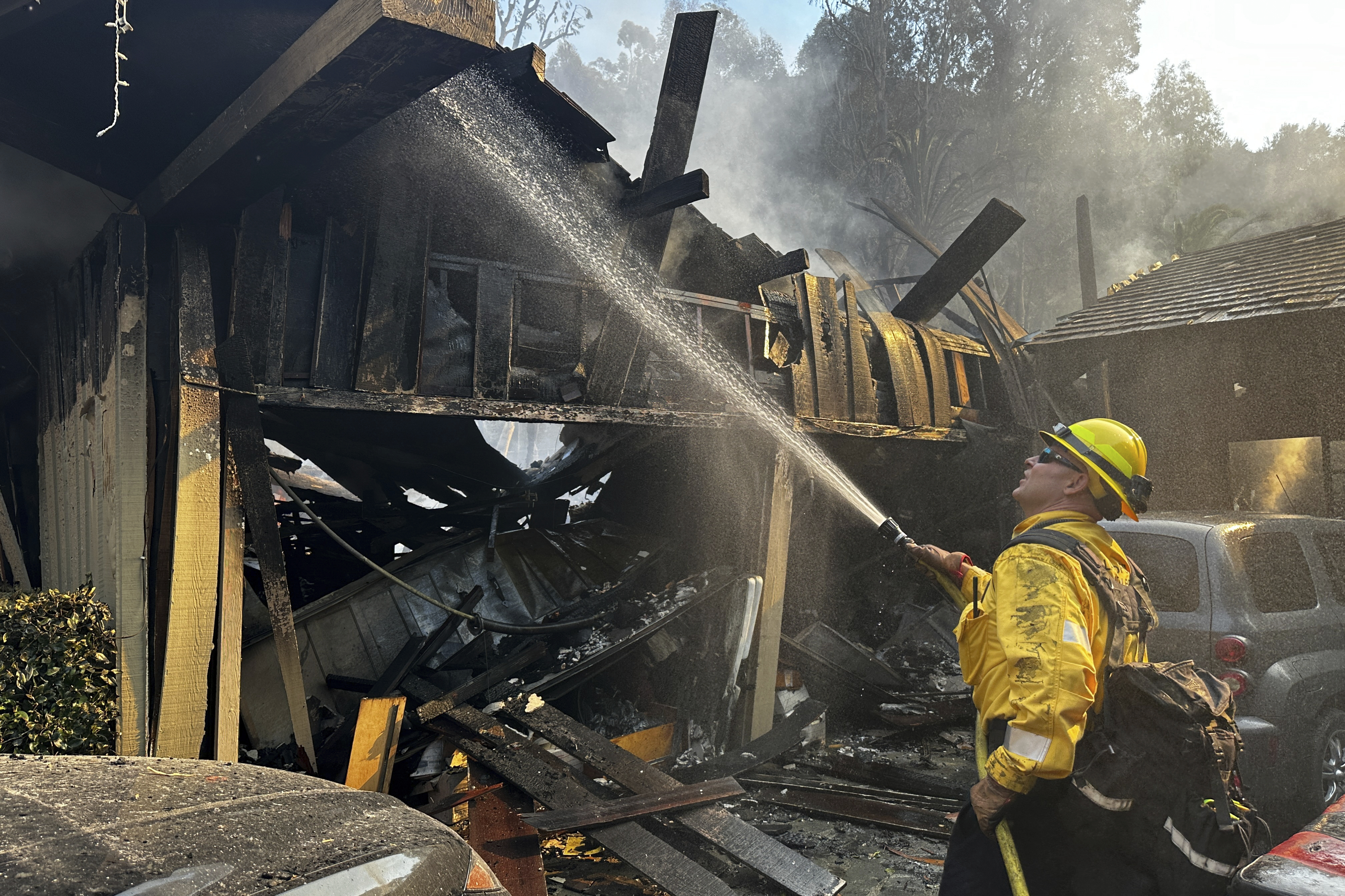 A firefighter hoses down hot spots around a fire-ravaged property after the Franklin Fire swept through Tuesday, Dec. 10, 2024, in Malibu, Calif. (AP Photo/Eugene Garcia)