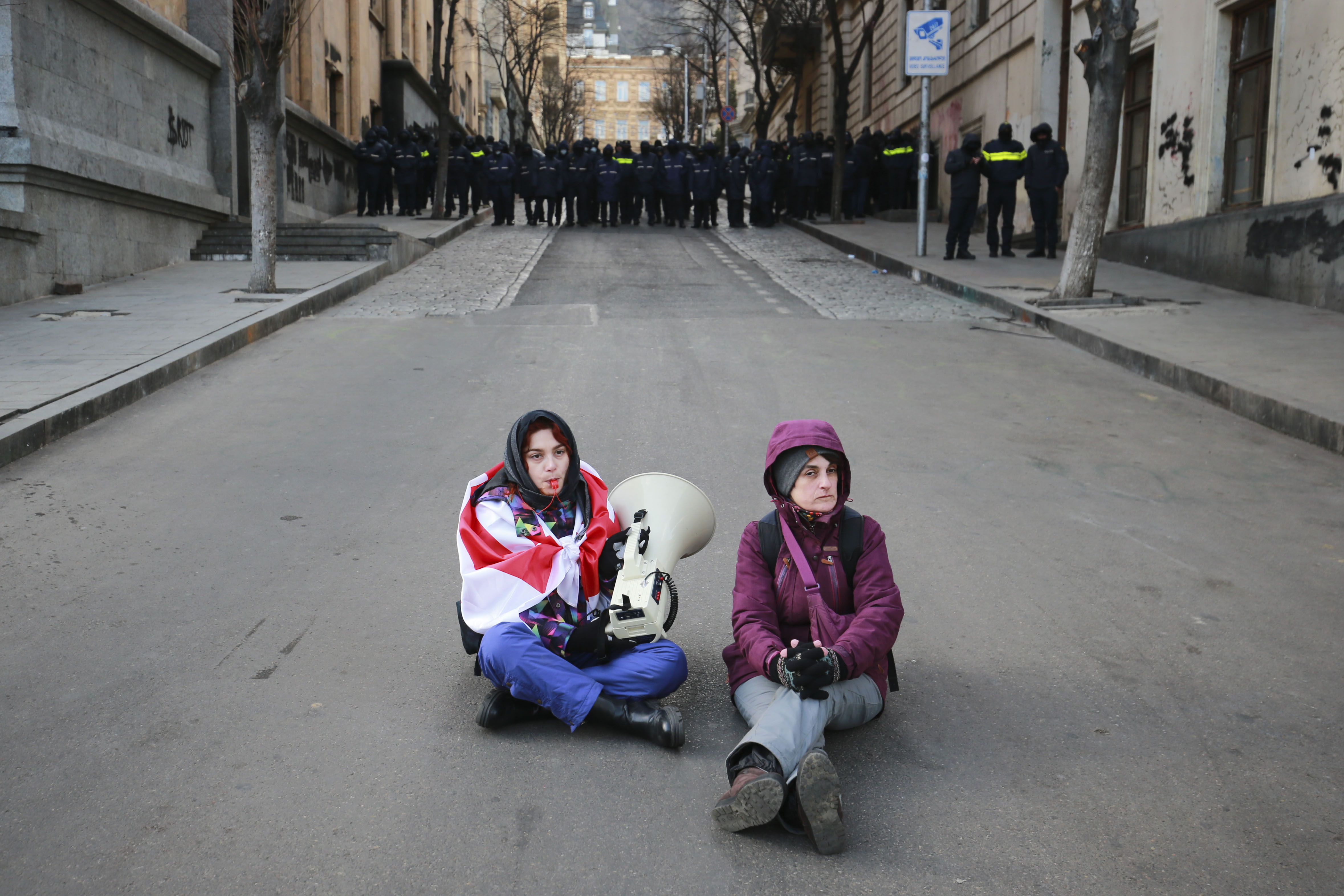 Protesters sit on a street as police block the street outside the Georgian parliament while the parliament has begun the procedure of the presidential elections, in Tbilisi, Georgia, Saturday, Dec. 14, 2024. (AP Photo/Zurab Tsertsvadze)