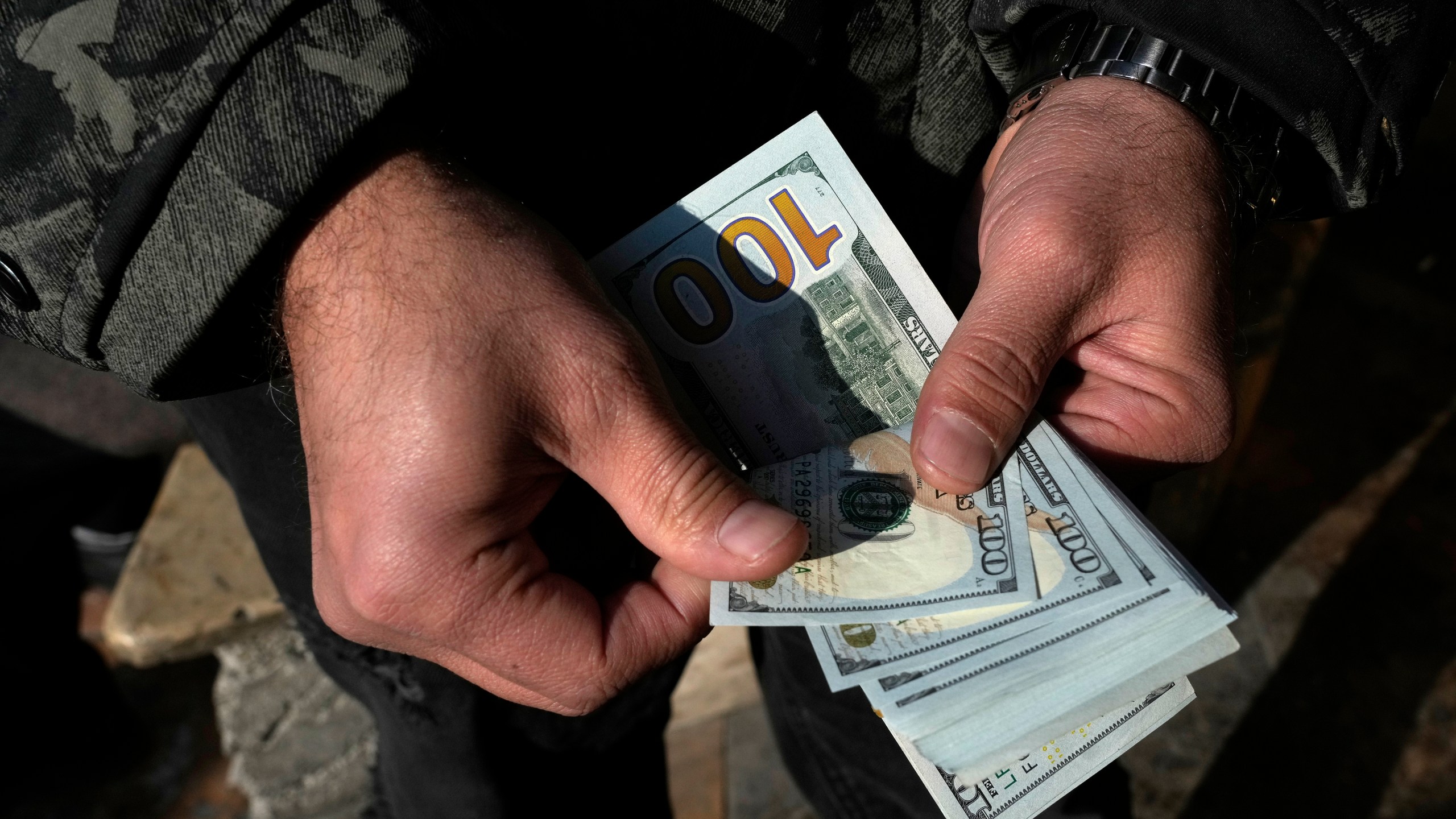 A man poses for a photo without showing his face as he counts U.S. dollars at Ferdowsi street, Tehran's go-to venue for foreign currency exchange, in downtown Tehran, Iran, Wednesday, Dec. 18, 2024. (AP Photo/Vahid Salemi)