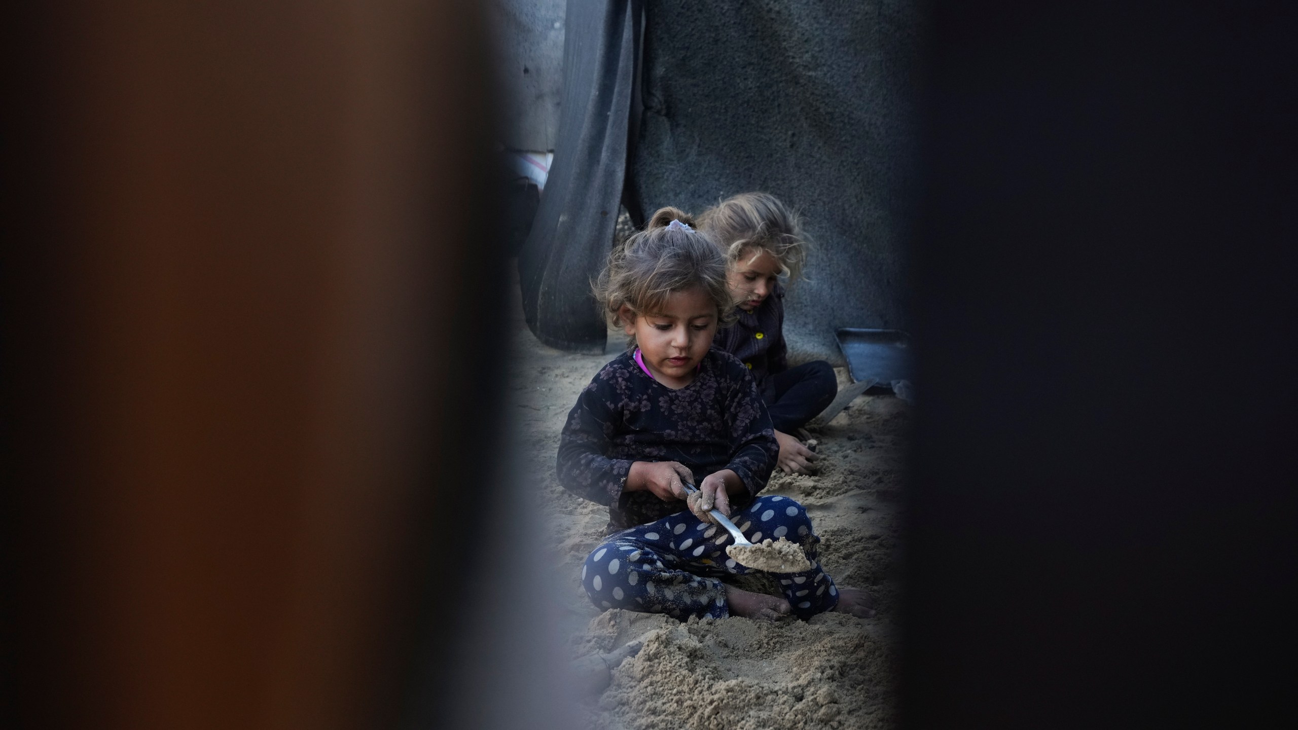 Grandchildren of Reda Abu Zarada, displaced from Jabaliya in northern Gaza, play with sand next to their tent at a camp in Khan Younis, Gaza Strip, Thursday, Dec. 19, 2024. (AP Photo/Abdel Kareem Hana)