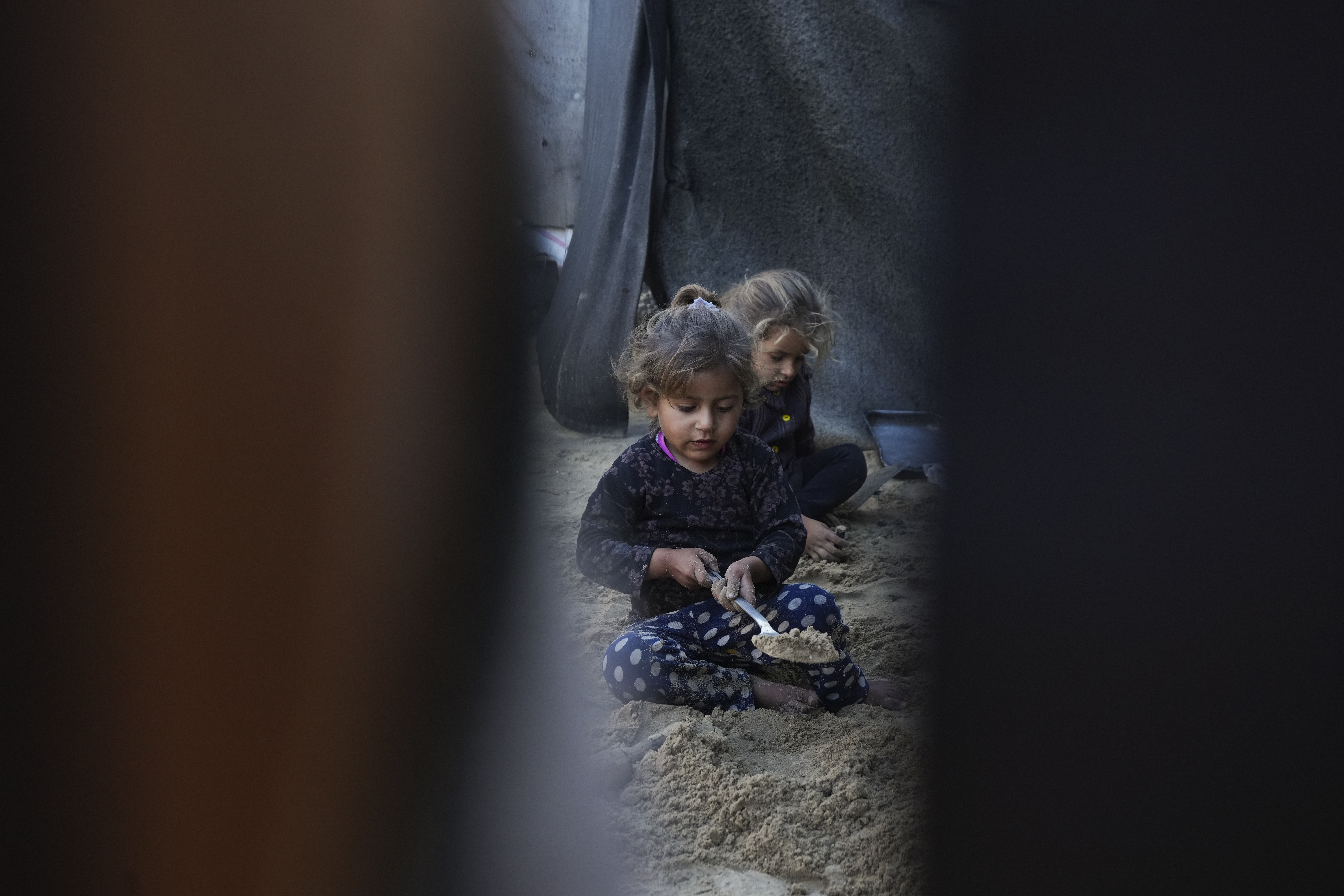 Grandchildren of Reda Abu Zarada, displaced from Jabaliya in northern Gaza, play with sand next to their tent at a camp in Khan Younis, Gaza Strip, Thursday, Dec. 19, 2024. (AP Photo/Abdel Kareem Hana)