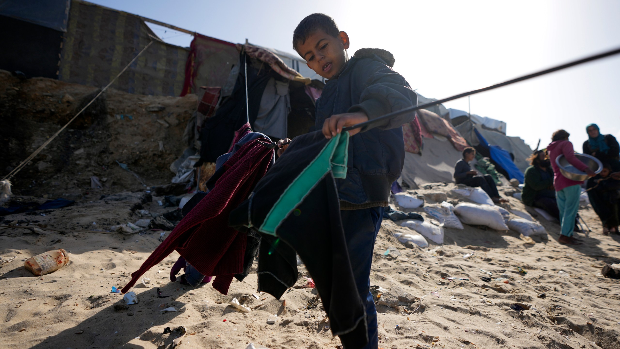 A Palestinian child hanging cloths on a rope outside tents made locally from pieces of cloth and nylon, in a camp for internally displaced Palestinians at the beachfront in Deir al-Balah, central Gaza Strip, Friday, Dec. 27, 2024. (AP Photo/Abdel Kareem Hana)