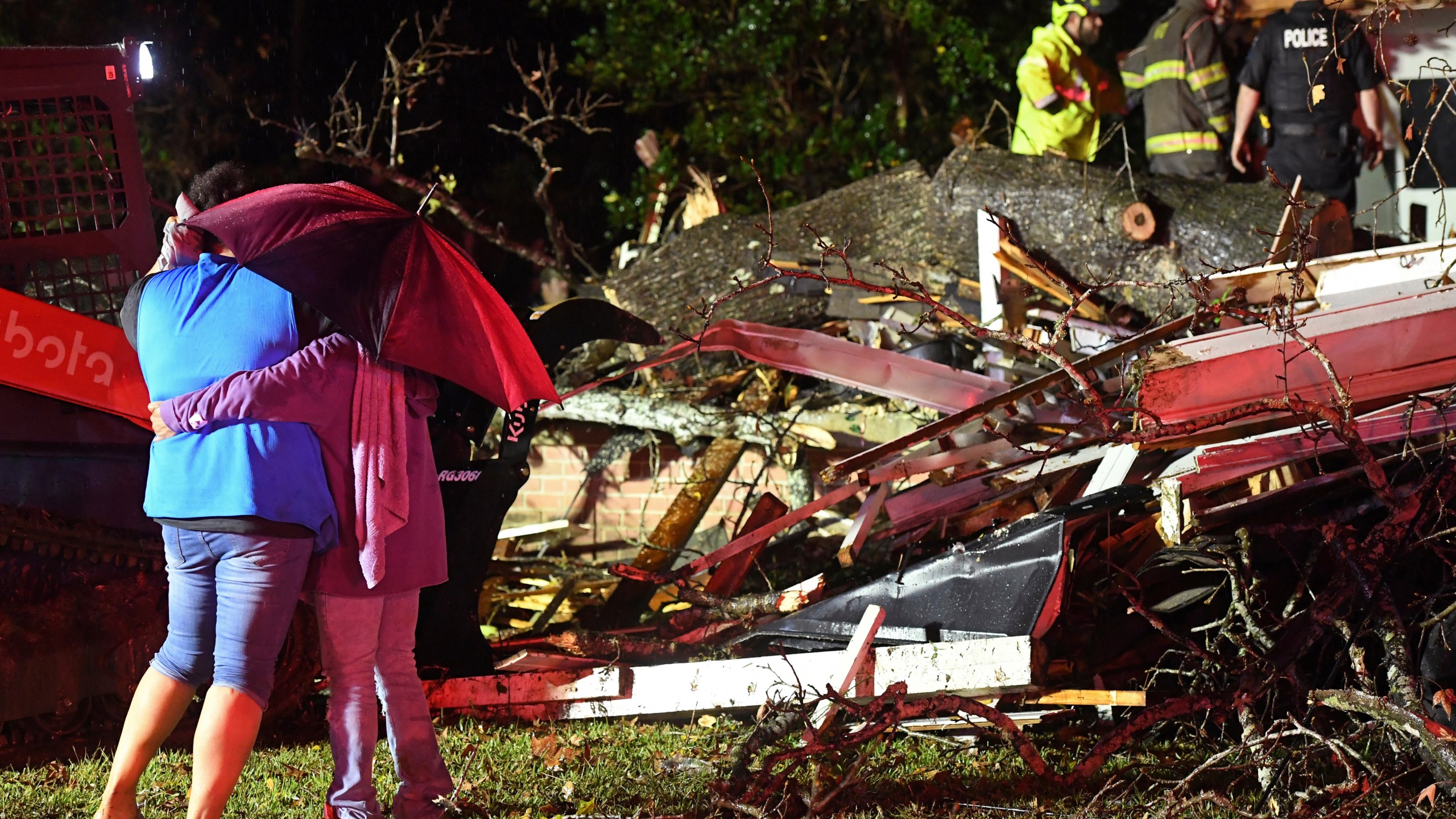 Bystanders hug as first responders work to free a victim after a tree fell on a house in Natchez, Miss., Saturday, Dec. 28, 2024. (Thomas Graning/The Natchez Democrat via AP)