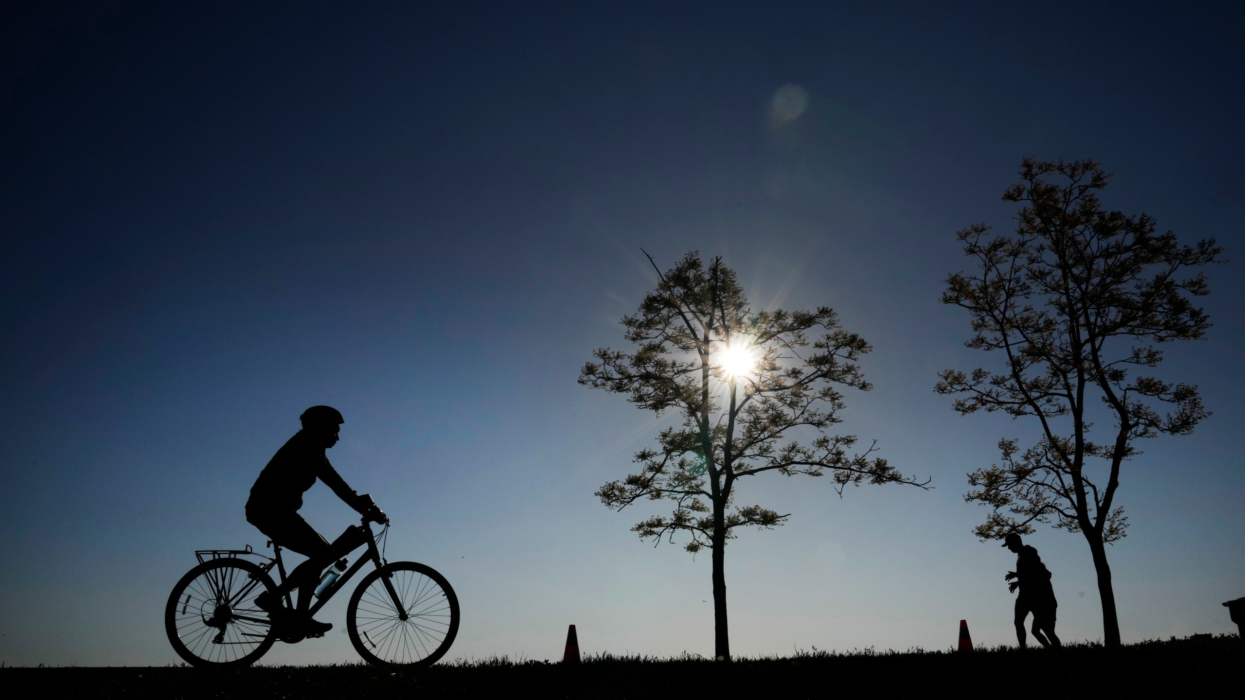 FILE - A cyclist and two joggers in silhouette navigate the bike path along Lake Michigan at the 31st Street Harbor Saturday, May 27, 2023, in Chicago. (AP Photo/Charles Rex Arbogast, File)