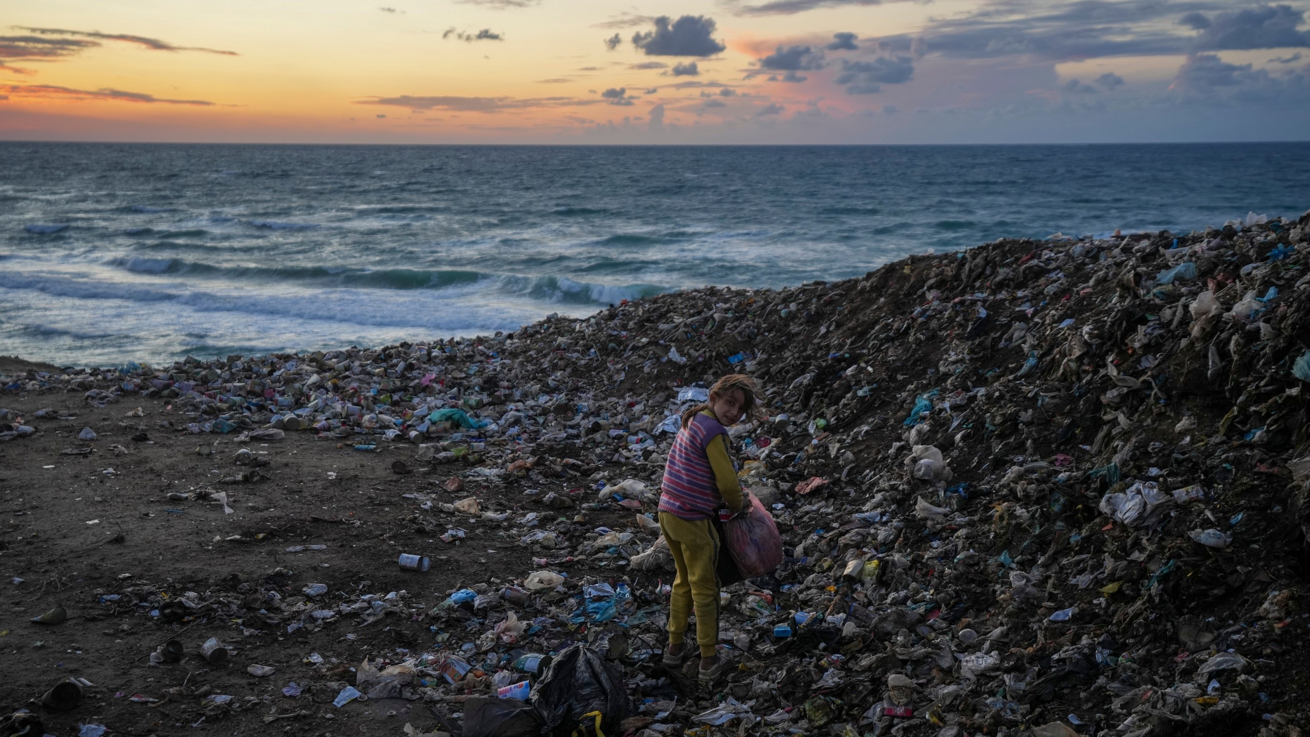 A girl searches for cardboard in the trash to make a fire, near a tent camp for displaced Palestinians by the sea in Deir al-Balah, central Gaza Strip, Monday, Dec. 30, 2024.