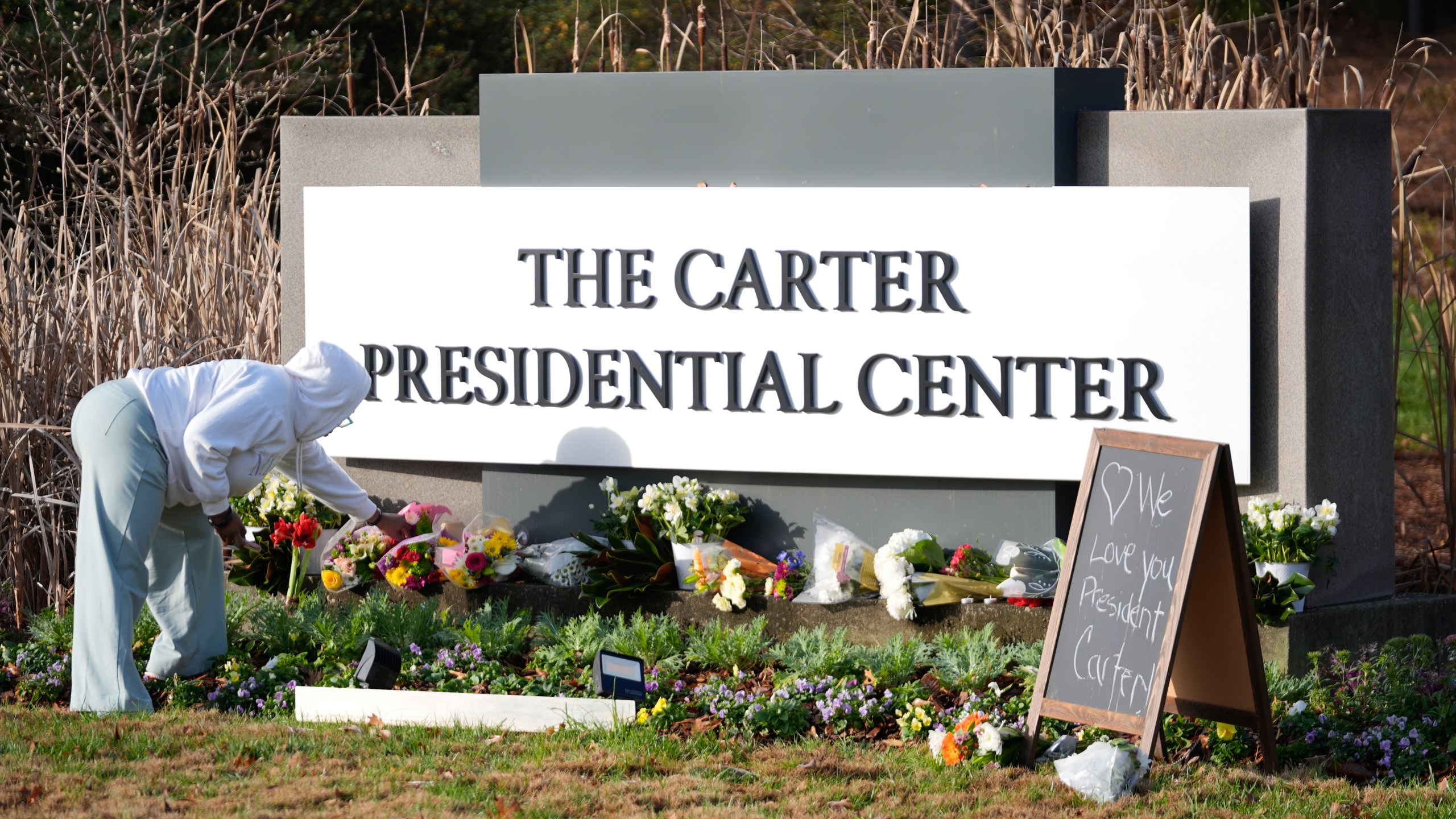 Christine Mason, of Atlanta, places flowers at entrance the The Jimmy Carter Presidential Center in Atlanta Monday, Dec. 30, 2024, in Atlanta. Formr President Jimmy Carter died Sunday at his home in Plains, Ga, at the age of 100. (AP Photo/John Bazemore )