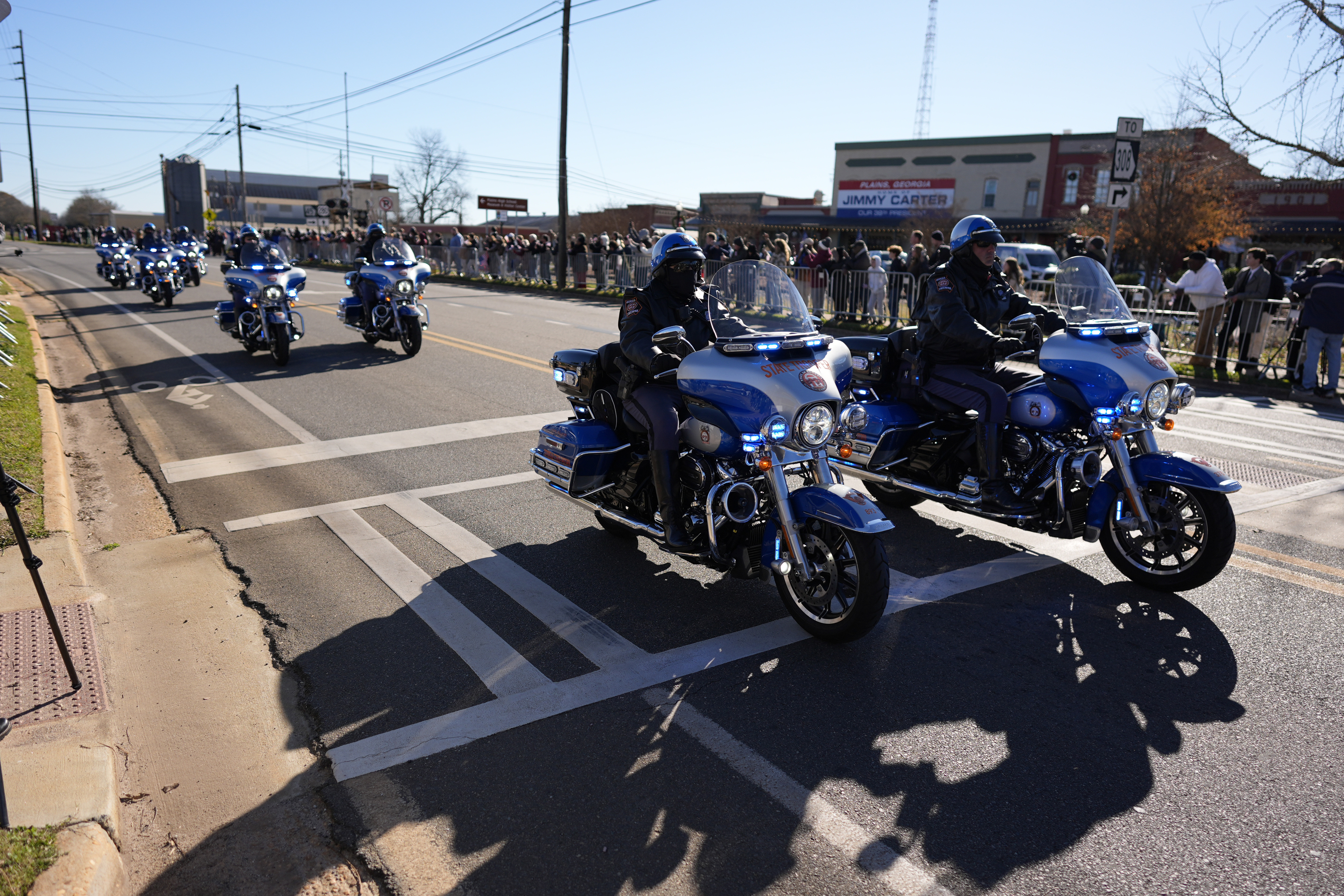 A police escort passes as the hearse carrying the flag-draped casket of former President Jimmy Carter approaches during a procession in downtown Plains, Ga., Saturday, Jan. 4, 2025. (AP Photo/Mike Stewart)