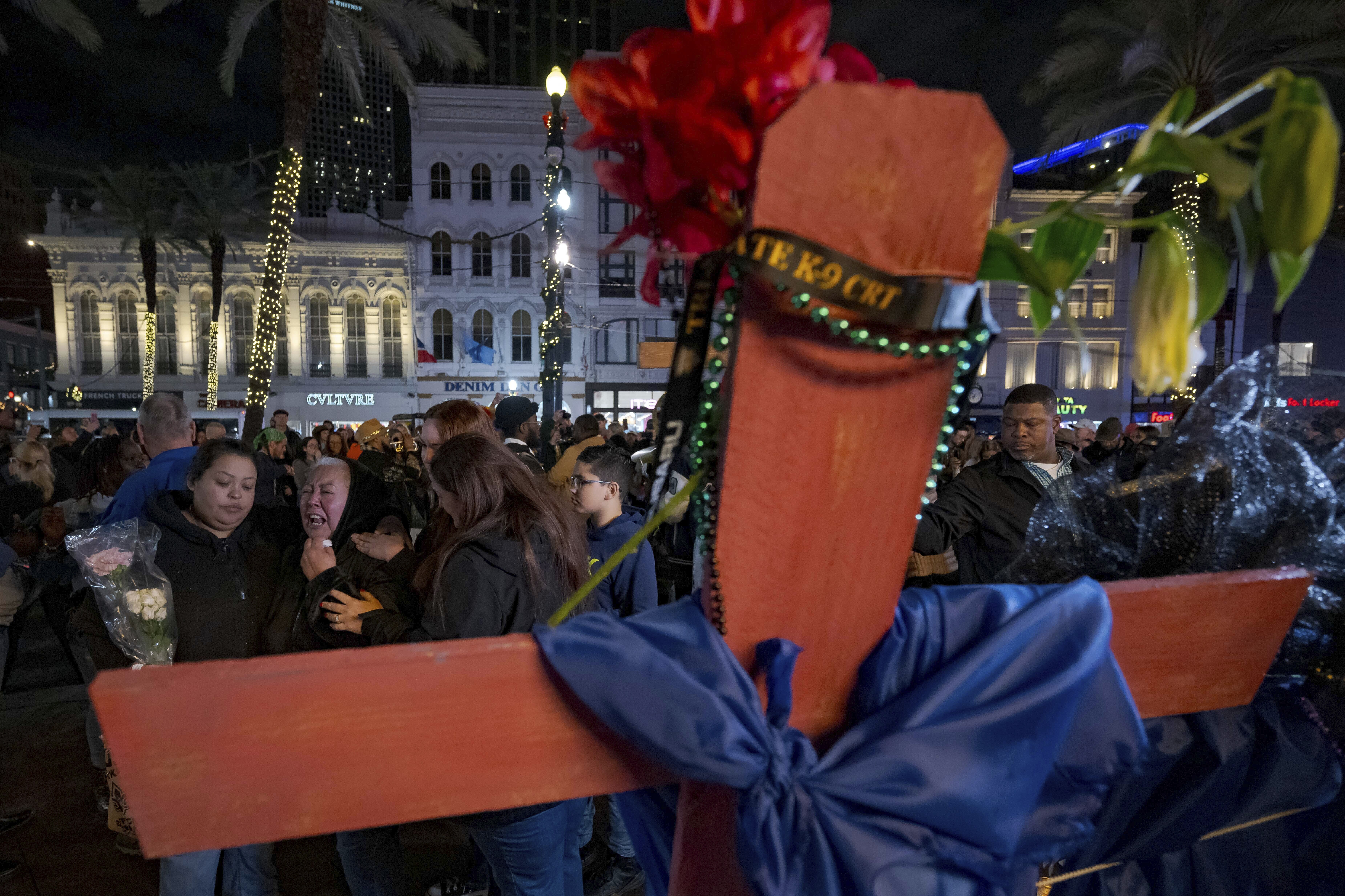 Jessica Perez, holding flowers left, hugs her mother Martha Perez who cries out by a cross memorializing her daughter, Nicole Perez, who was a victim on the New Year's Day attack, on Canal Street near the intersection of Bourbon Street in New Orleans, Saturday, Jan. 4, 2025. (AP Photo/Matthew Hinton)