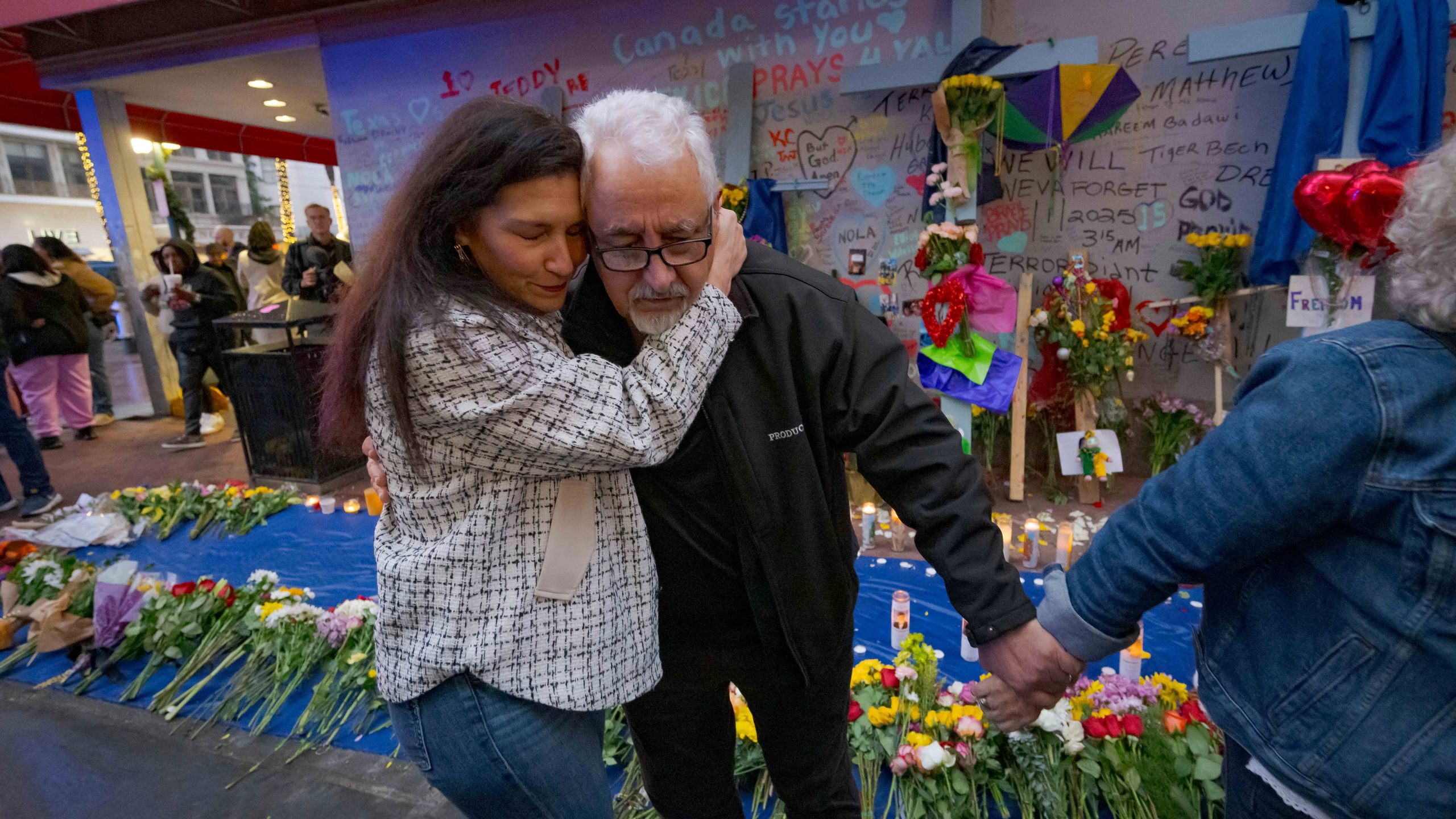 Long Island, New York residents Louis Tenedorio is hugged by family friend Angelique Whittington, left, while holding the hand of his wife, Cathy Tenedorio, by a memorial Bourbon Street and Canal Street in New Orleans, Saturday, Jan. 4, 2025, where their son, Matthew Tenedorio, was killed as one of the victims of the New Year's Day deadly truck attack and shooting. (AP Photo/Matthew Hinton)