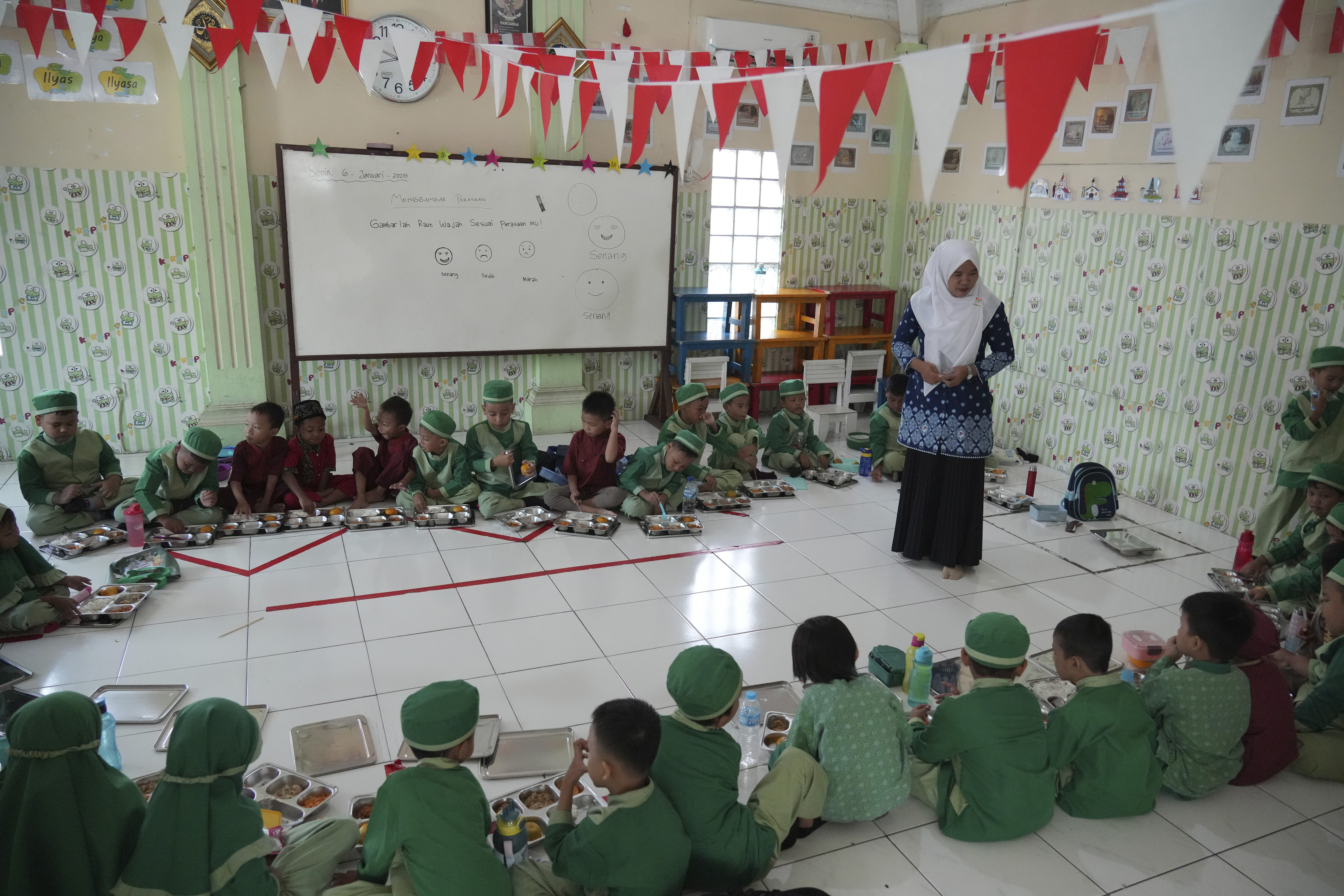 Students sit on the floor as they have their meals during the kick off of President Prabowo Subianto's ambitious free meal program to feed children and pregnant women nationwide despite critics saying that its required logistics could hurt Indonesia's state finances and economy at Early Childhood Education and Development in Jakarta, Indonesia, Monday, Jan. 6, 2025. (AP Photo/Achmad Ibrahim)