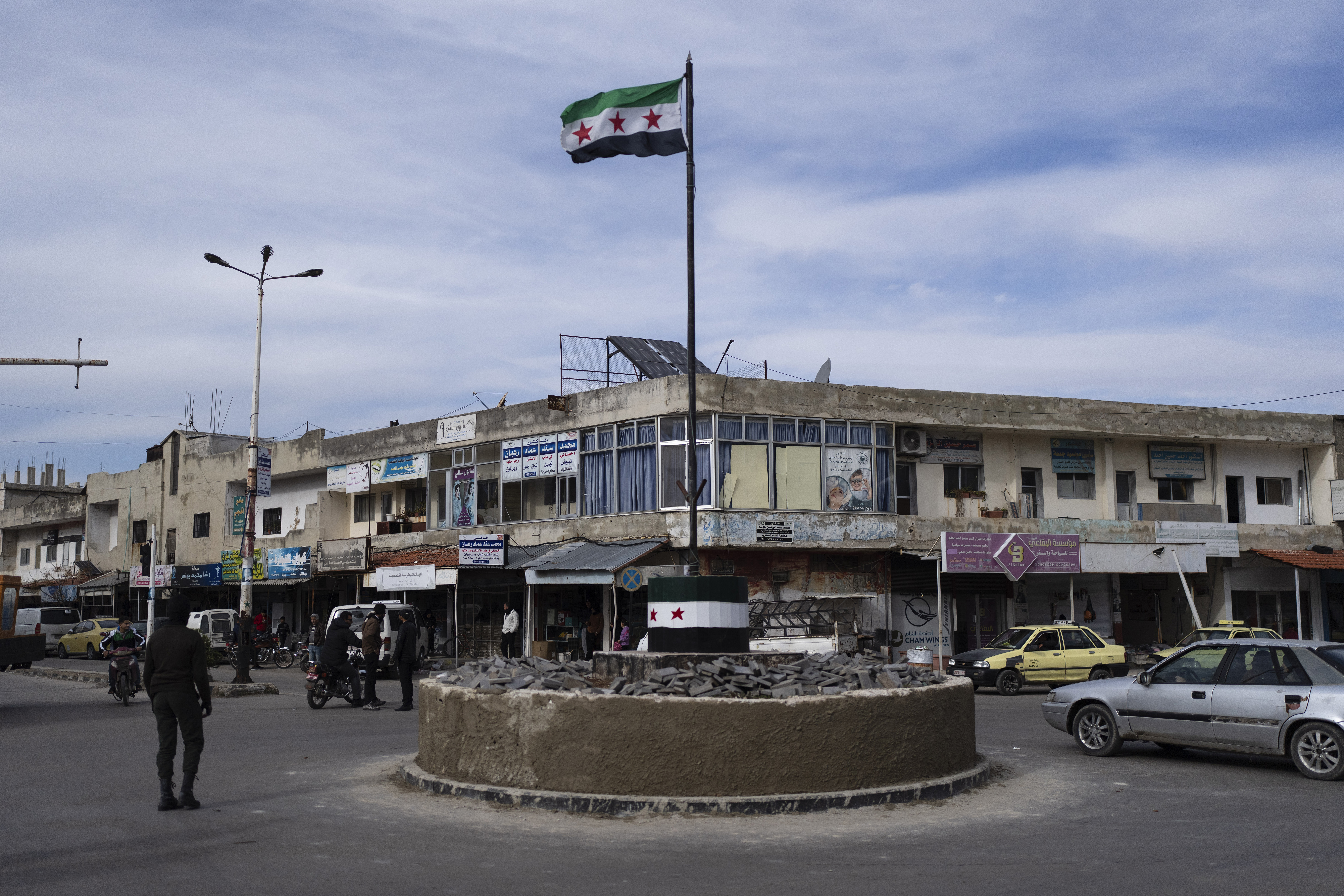 Cars drive past a roundabout hoisting the new Syrian flag after the ousting of the Assad regime, in Salam City, formerly called Baath City after the ruling party, in Quneitra, Syria, Sunday, Jan. 5, 2025. (AP Photo/Mosa'ab Elshamy)