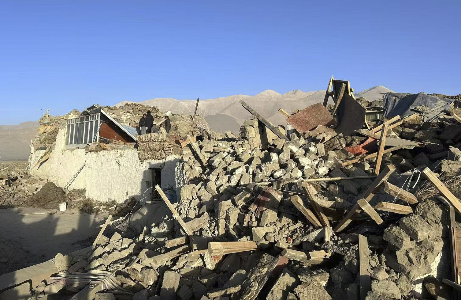 In this photo released by Xinhua News Agency, people stand amidst damaged houses in the aftermath of an earthquake in Tonglai Village, Changsuo Township of Dingri in Xigaze, southwestern China's Tibet Autonomous Region on Tuesday, Jan. 7, 2025. (Xinhua via AP)