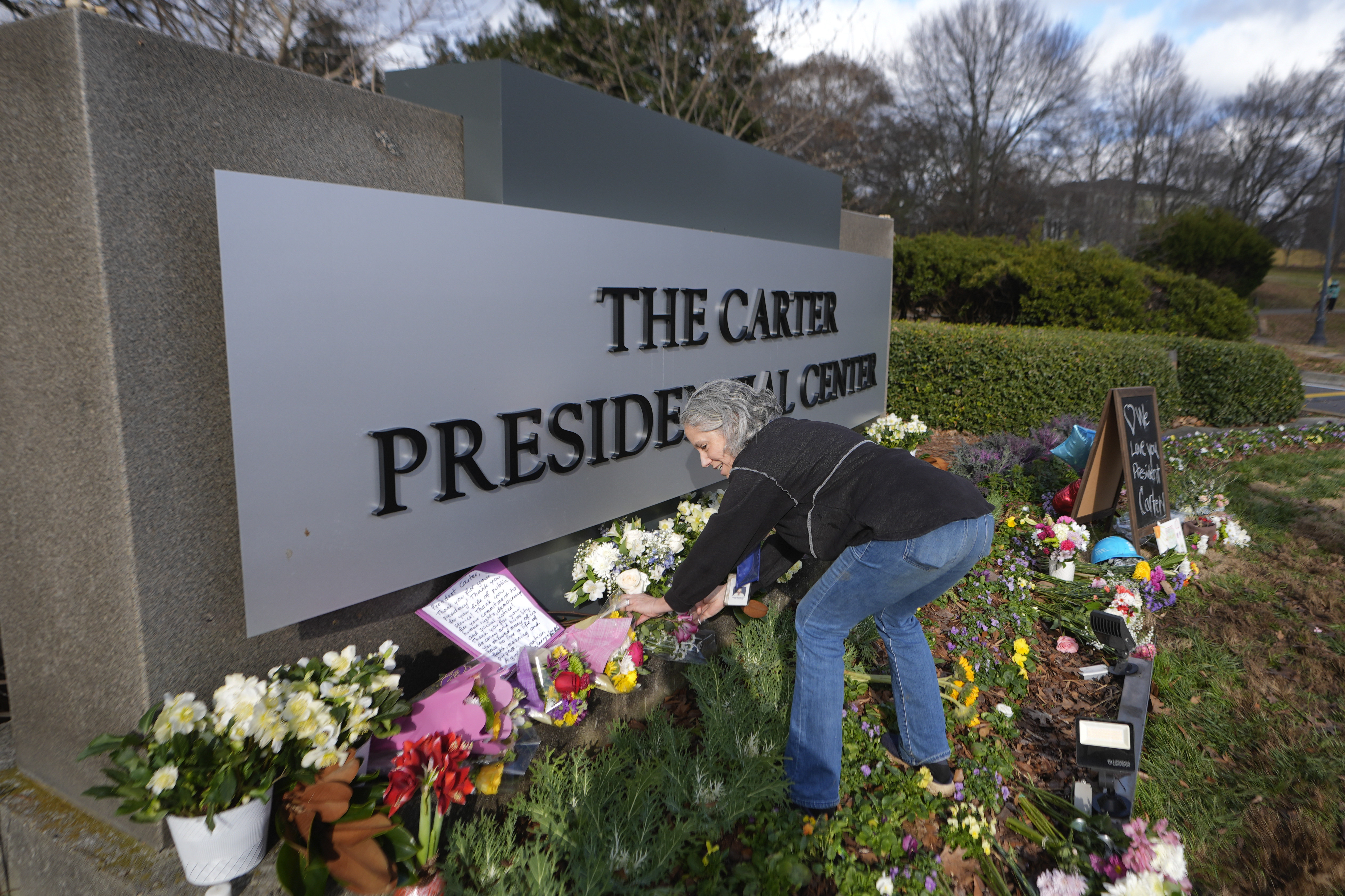 Carter Center volunteer Denise Bomberger places flowers at the entrance to the Jimmy Carter Presidential Center Tuesday, Dec. 31, 2024, in Atlanta. Carter died Sunday at he age of 100. (AP Photo/John Bazemore )