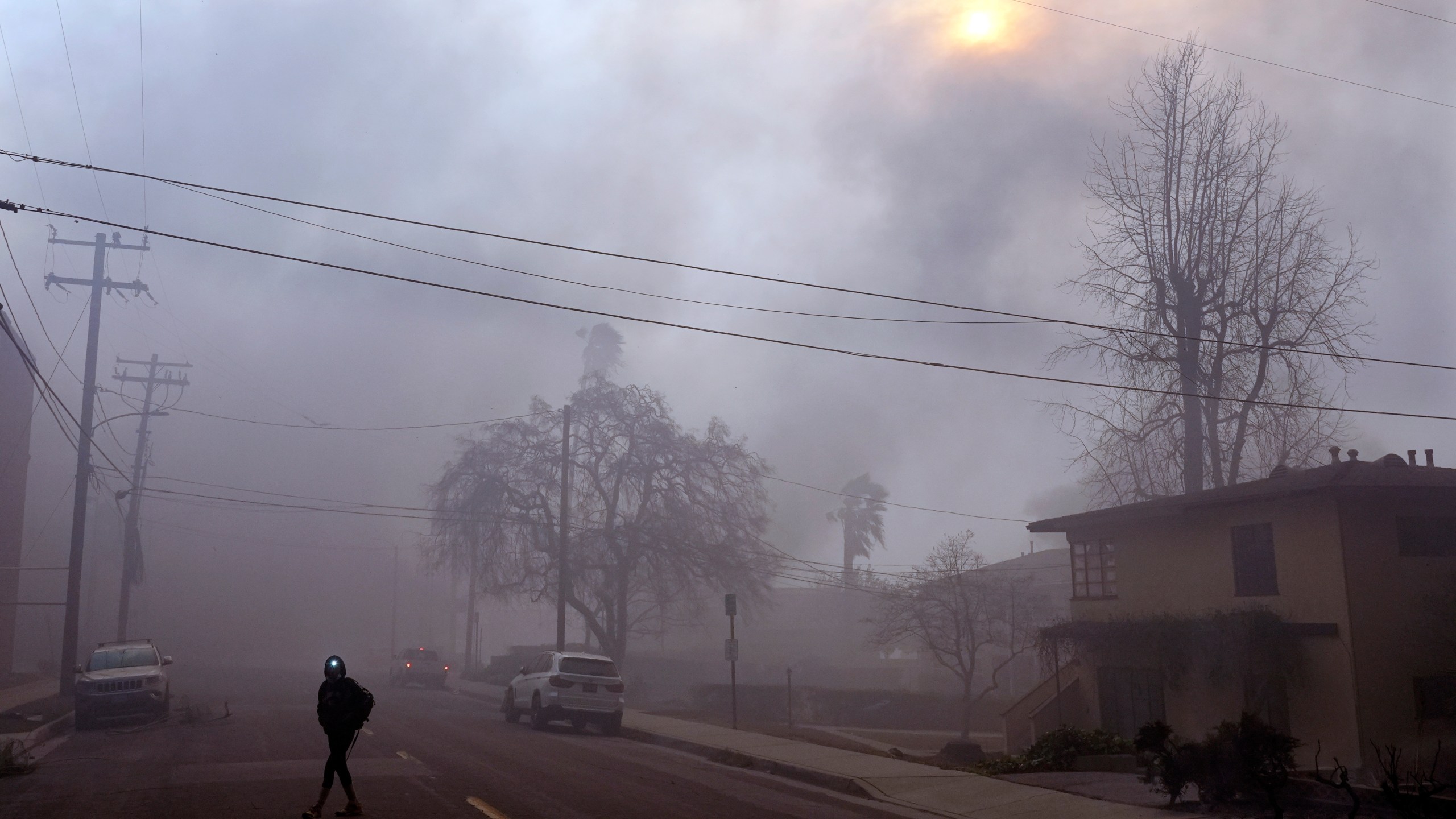 A pedestrian uses a flashlight to make his way down a smoke-filled street during wildfires in the Altadena section of Pasadena, Calif., Wednesday, Jan. 8, 2025. (AP Photo/Chris Pizzello)