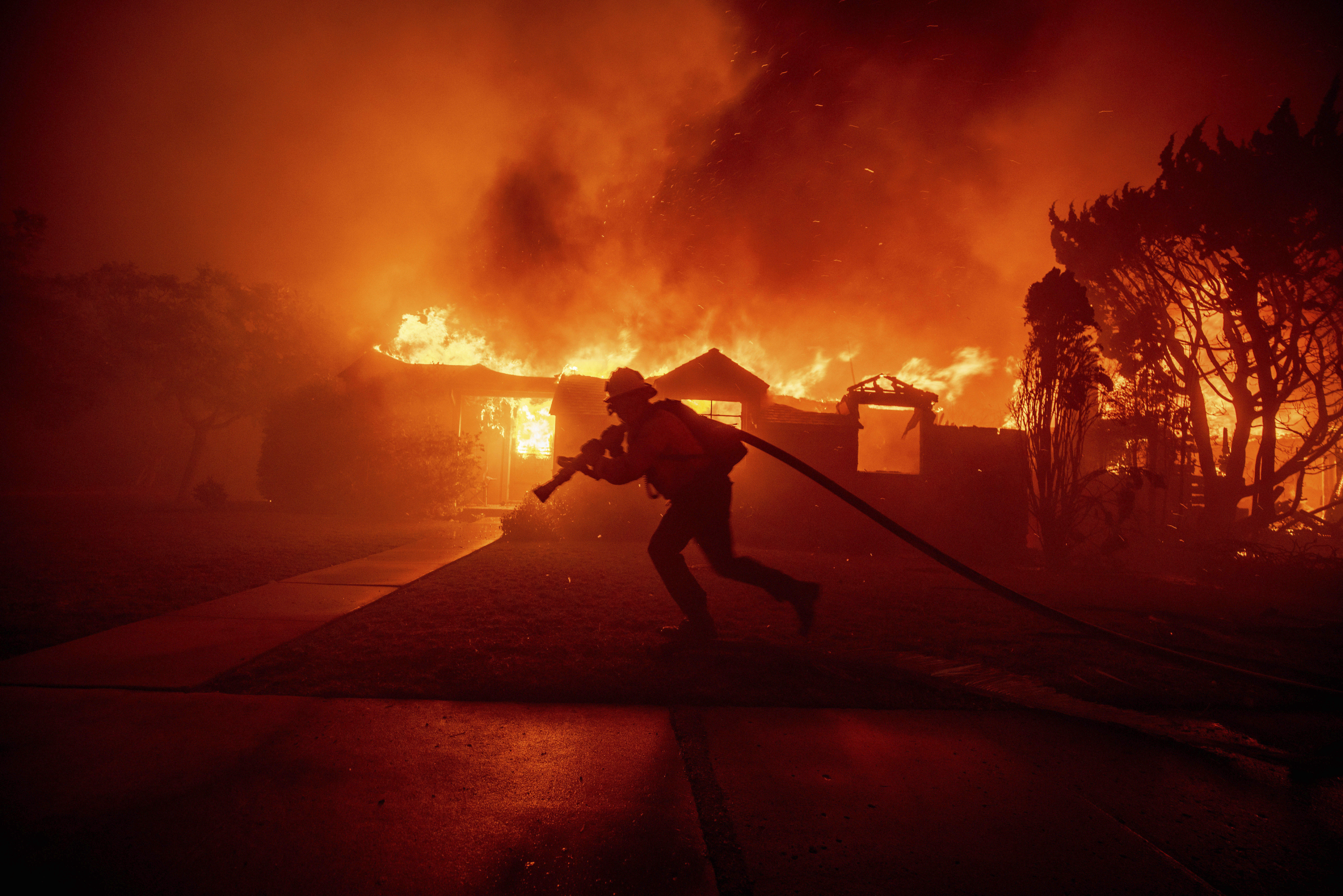 A firefighter battles the Palisades Fire as it burns a structure in the Pacific Palisades neighborhood of Los Angeles, Tuesday, Jan. 7, 2025. (AP Photo/Ethan Swope)