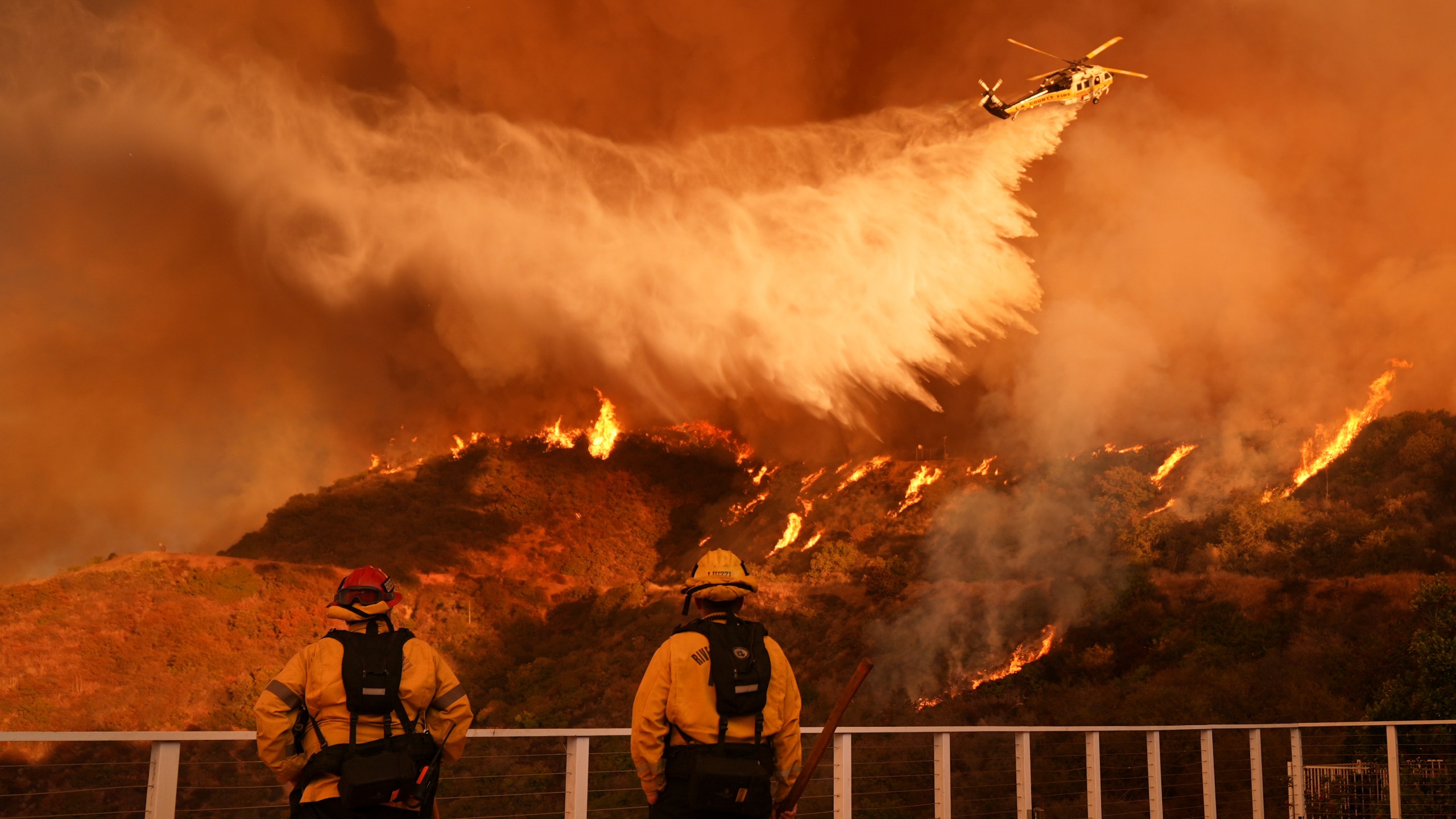 Firefighters watch as water is dropped on the Palisades Fire in Mandeville Canyon Saturday, Jan. 11, 2025, in Los Angeles. (AP Photo/Jae C. Hong)