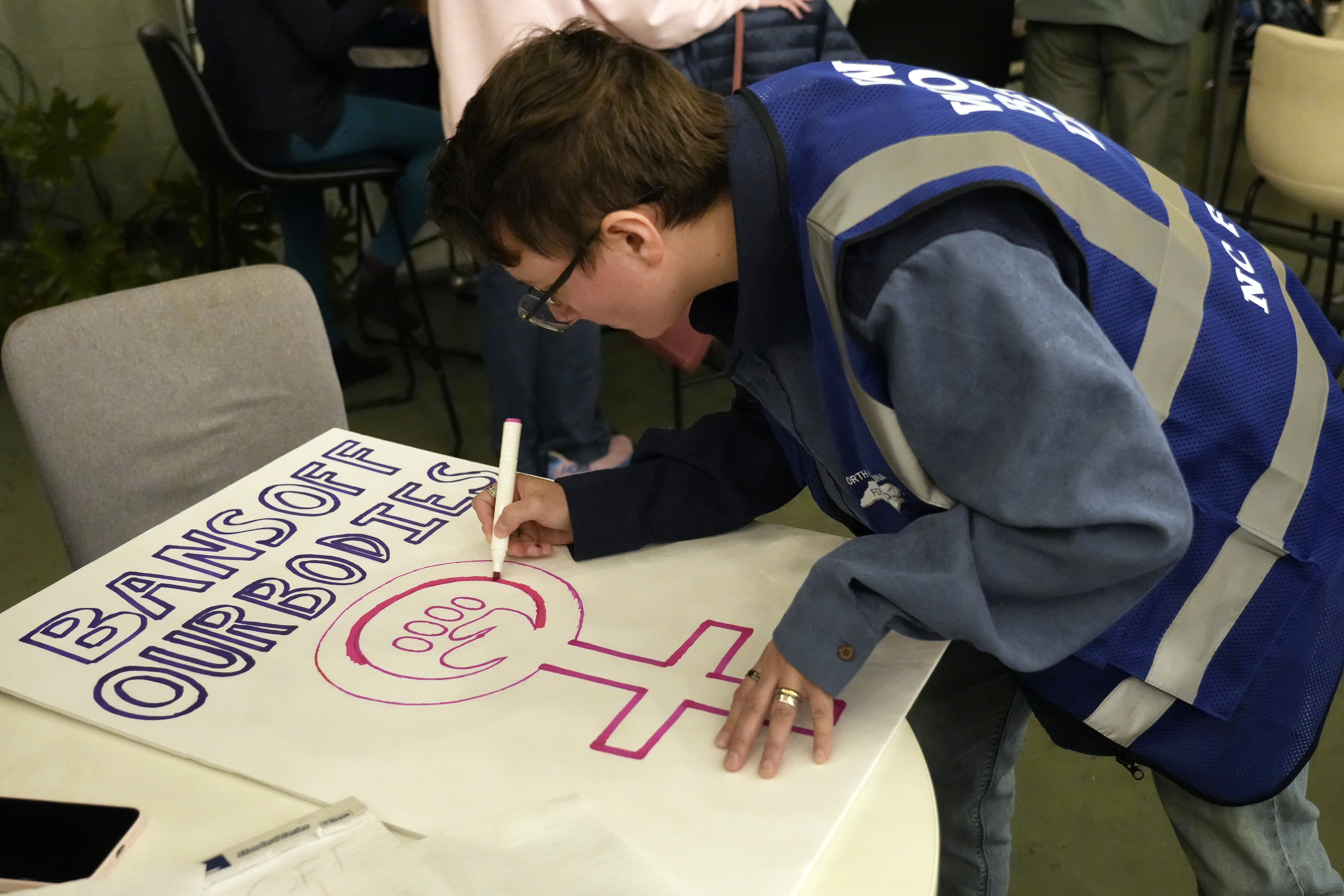 Cole Archer works on a protest sign during a meeting of NC Forward in High Point, N.C., Tuesday, Jan. 14, 2025. The group is traveling to Washington to take part in the People's March on Jan. 18 ahead of the inauguration. (AP Photo/Chuck Burton)