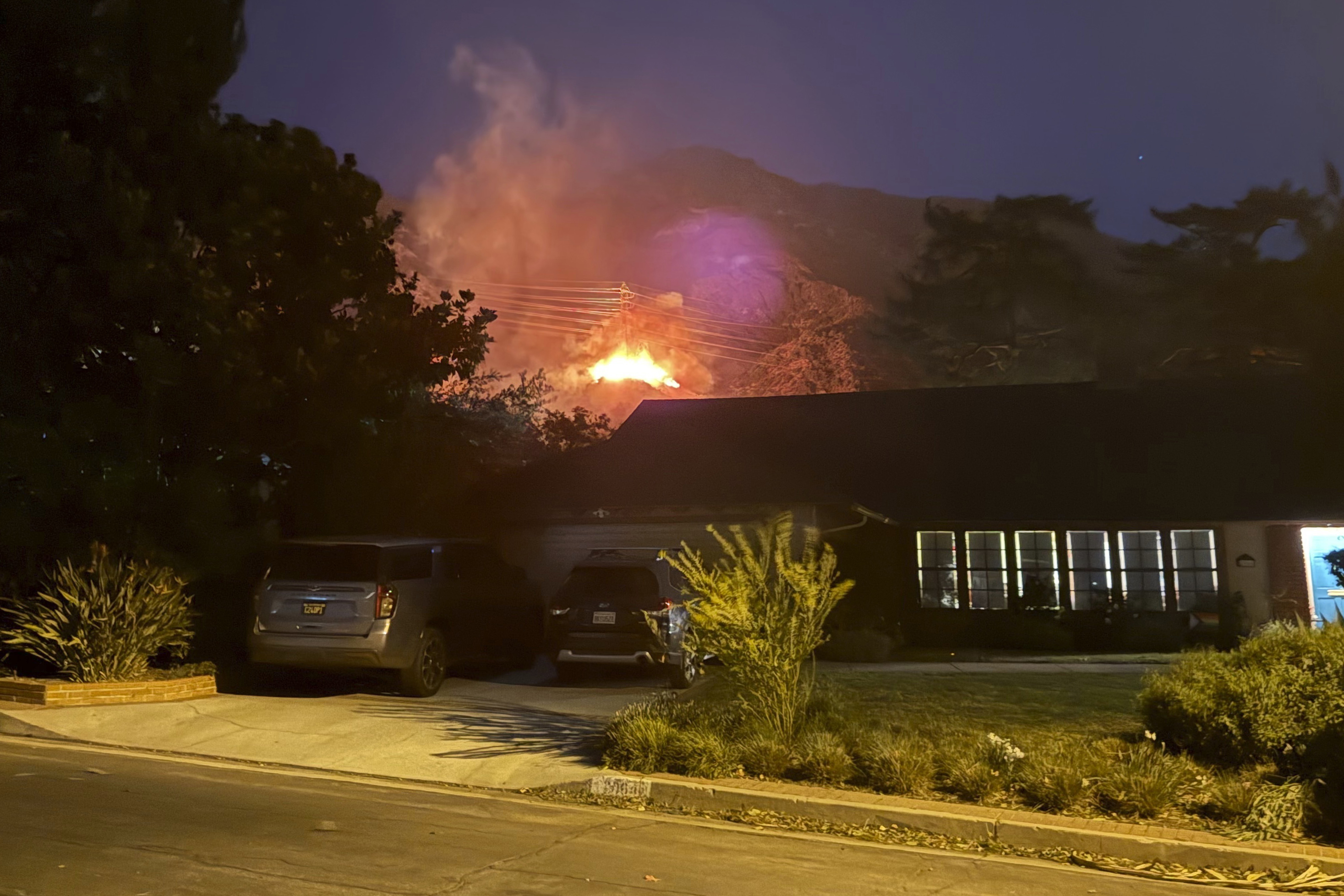 In this photo provided by Pasadena, Calif., resident Matt Logelin, flames burn beneath transmission towers owned by Southern California Edison in Eaton Canyon in the early evening of Tuesday, Jan. 7, 2025. (Matt Logelin via AP)