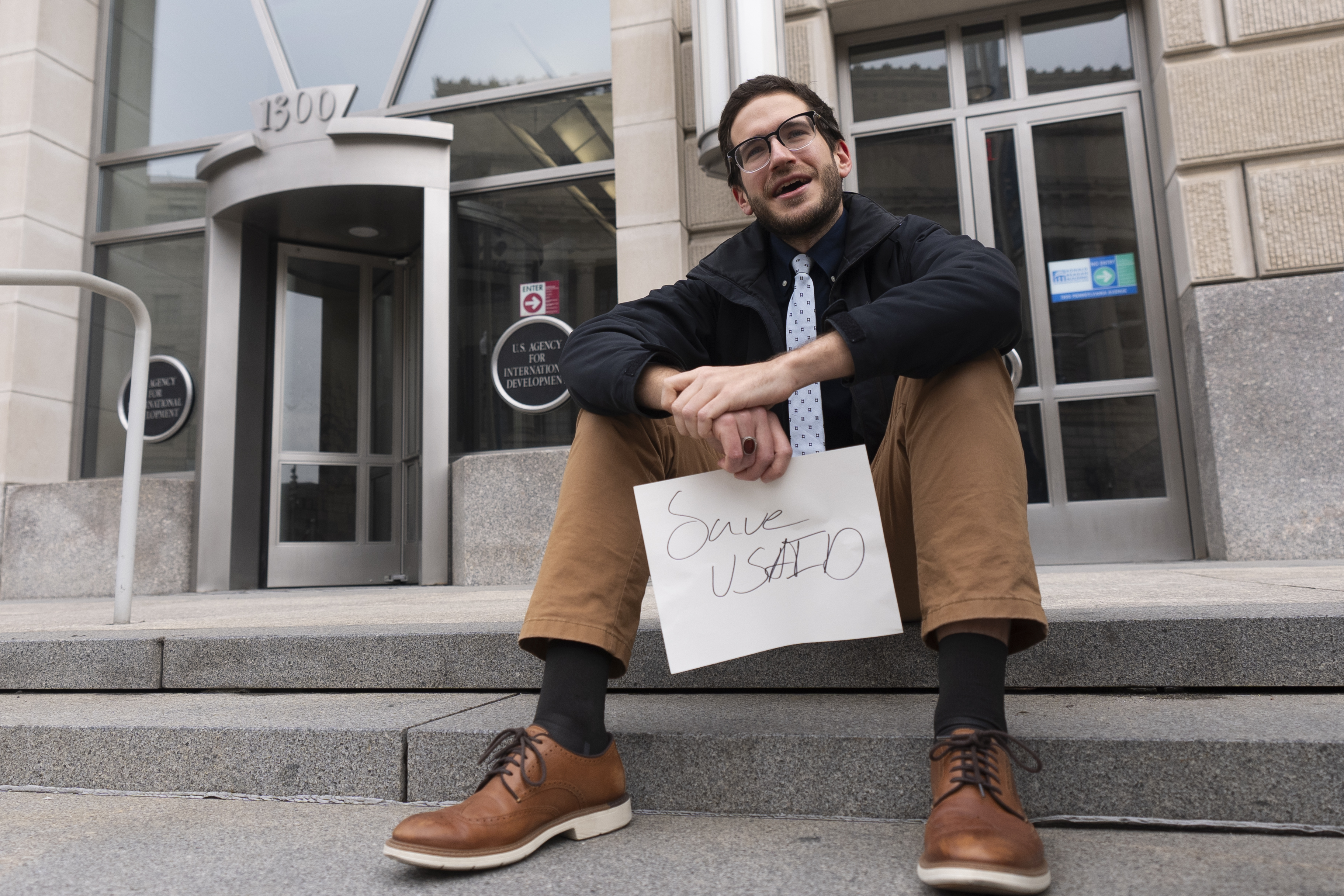 A United States Agency for International Development, or USAID, contract worker sits in front of the USAID office with a message written on a piece of paper, Monday, Feb. 3, 2025, in Washington (AP Photo/Manuel Balce Ceneta)