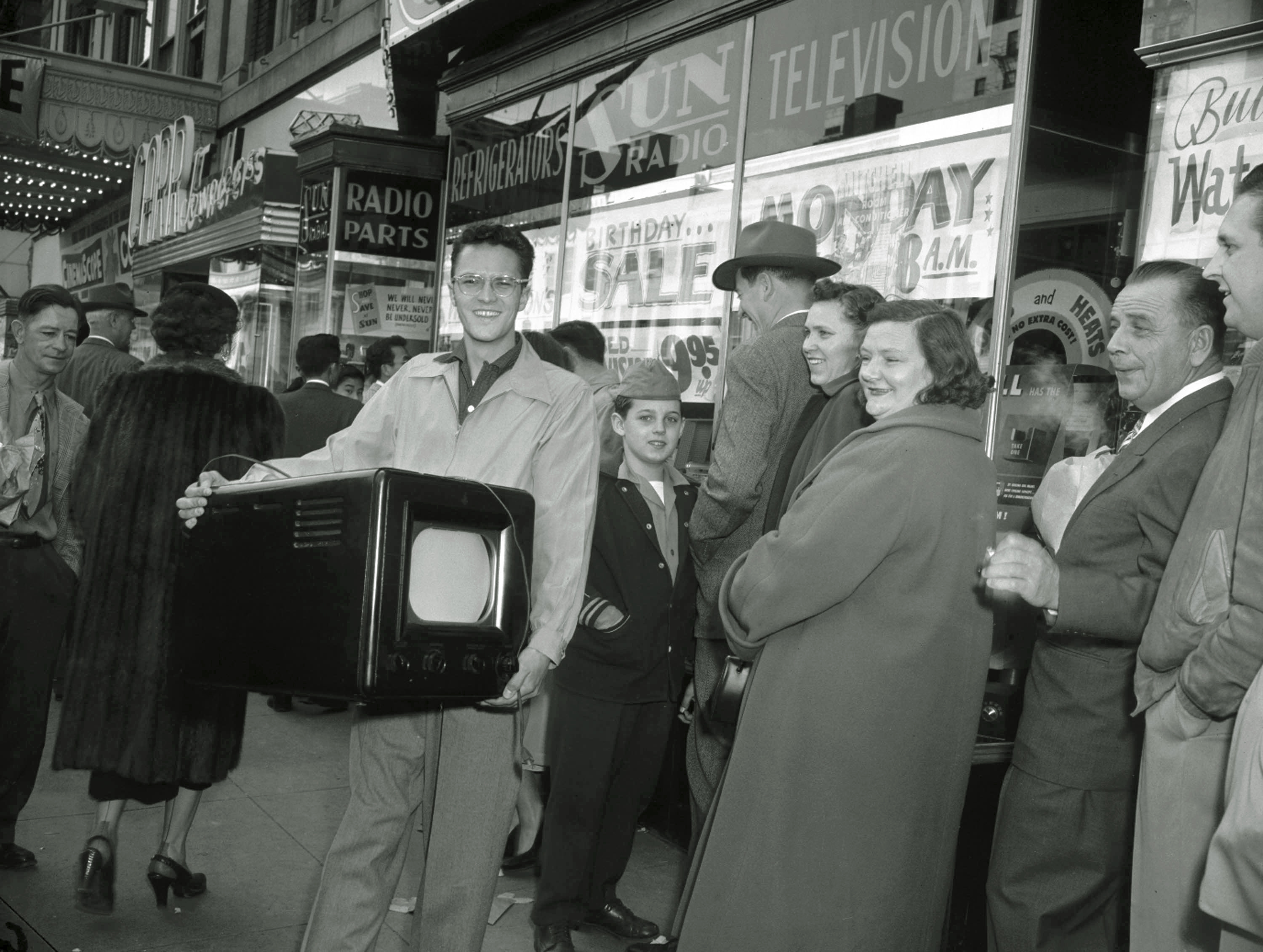 FILE - Phil Bustos of Trinidad, Colo., displays the television set he bought for $29 at a Washington's Birthday sale in Washington, D.C., Feb. 22, 1954. Other bargain hunters waited to get into the packed store during the annual holiday sale. (AP Photo, File)