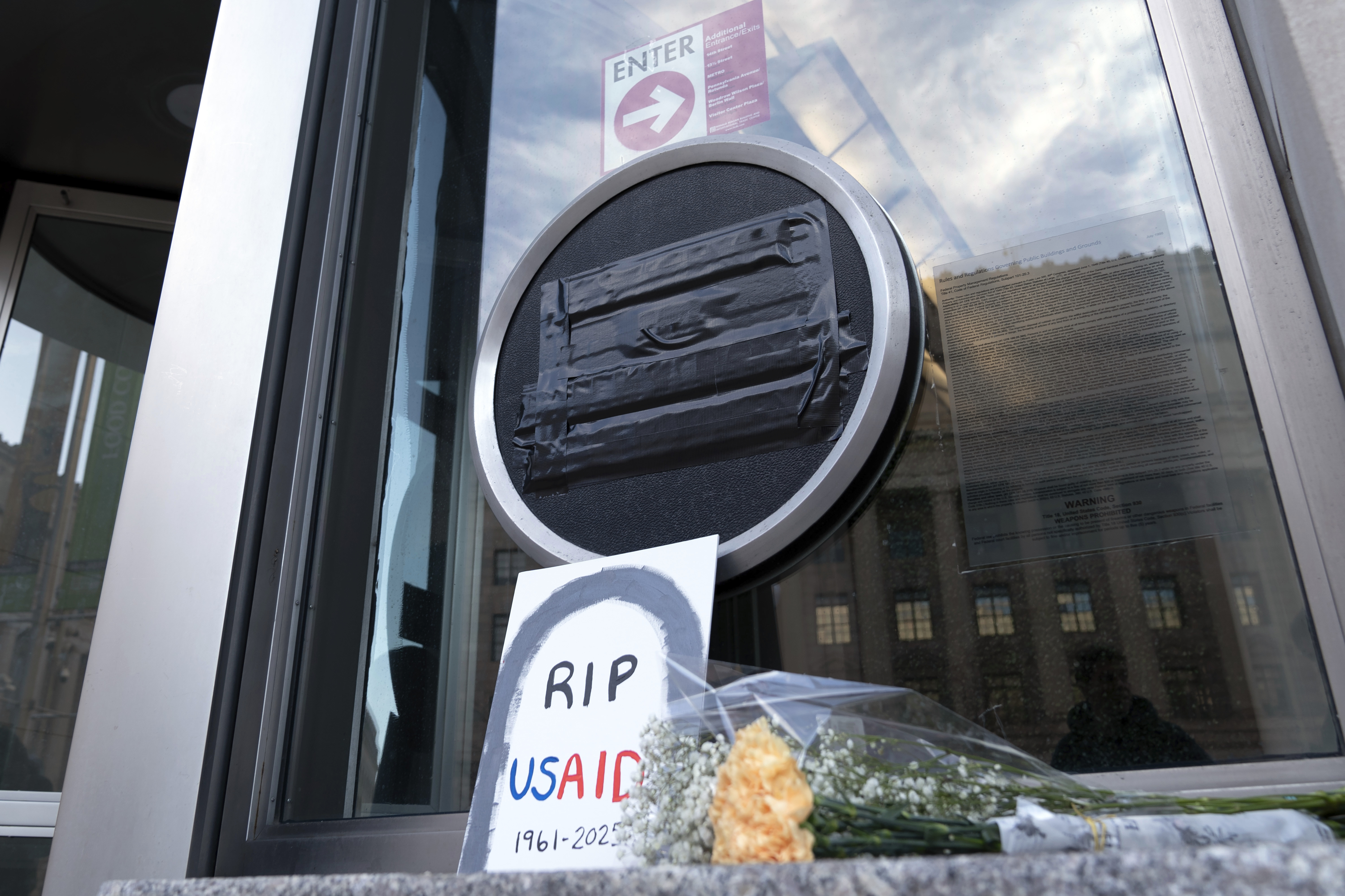 FILE - Flowers and a sign are placed outside the headquarters of the U.S. Agency for International Development, or USAID, Feb. 7, 2025, in Washington. (AP Photo/Jose Luis Magana, file)